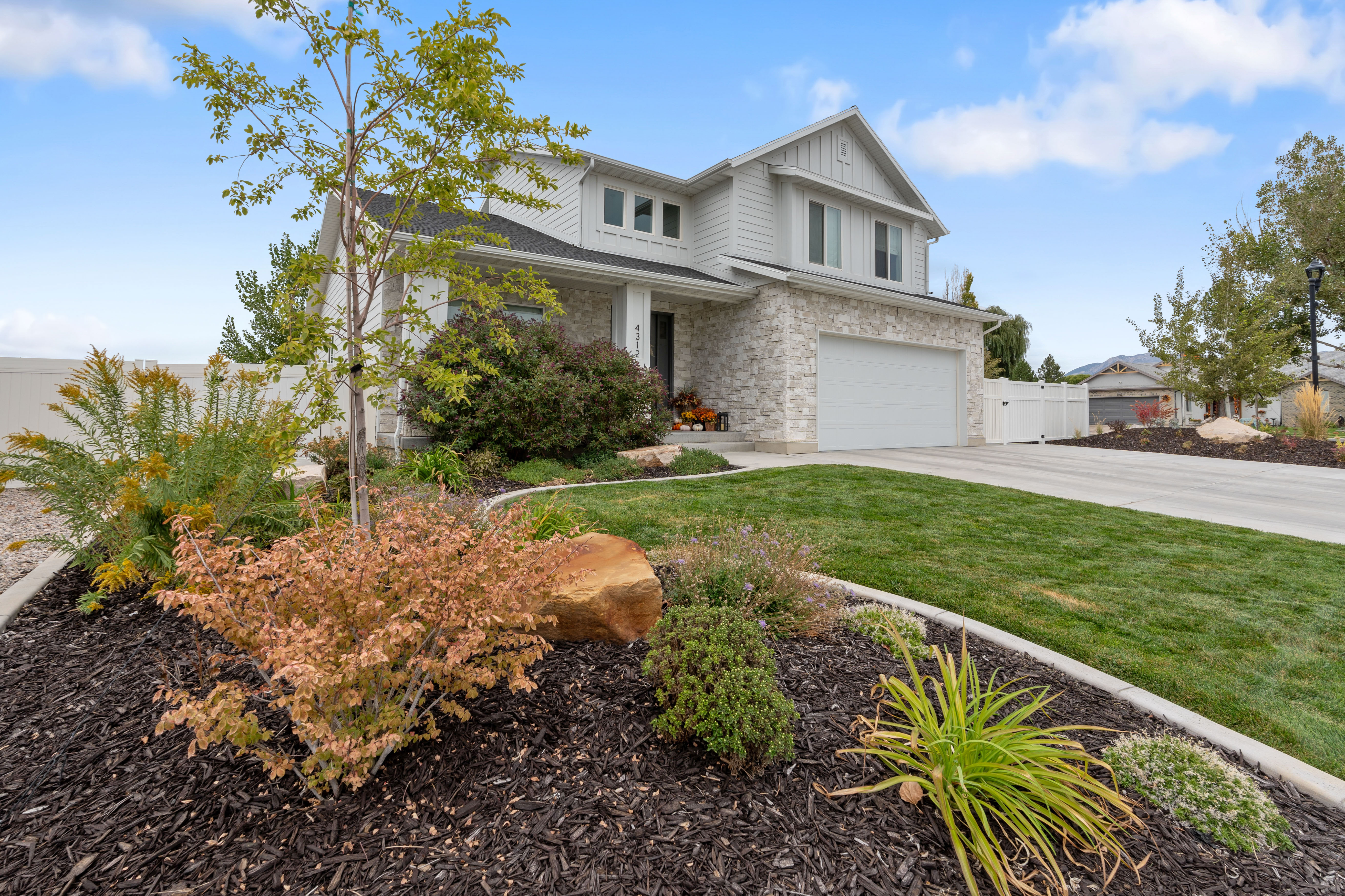 Contemporary two-story residence featuring a white siding and stone façade, a two-car garage, and a concrete driveway