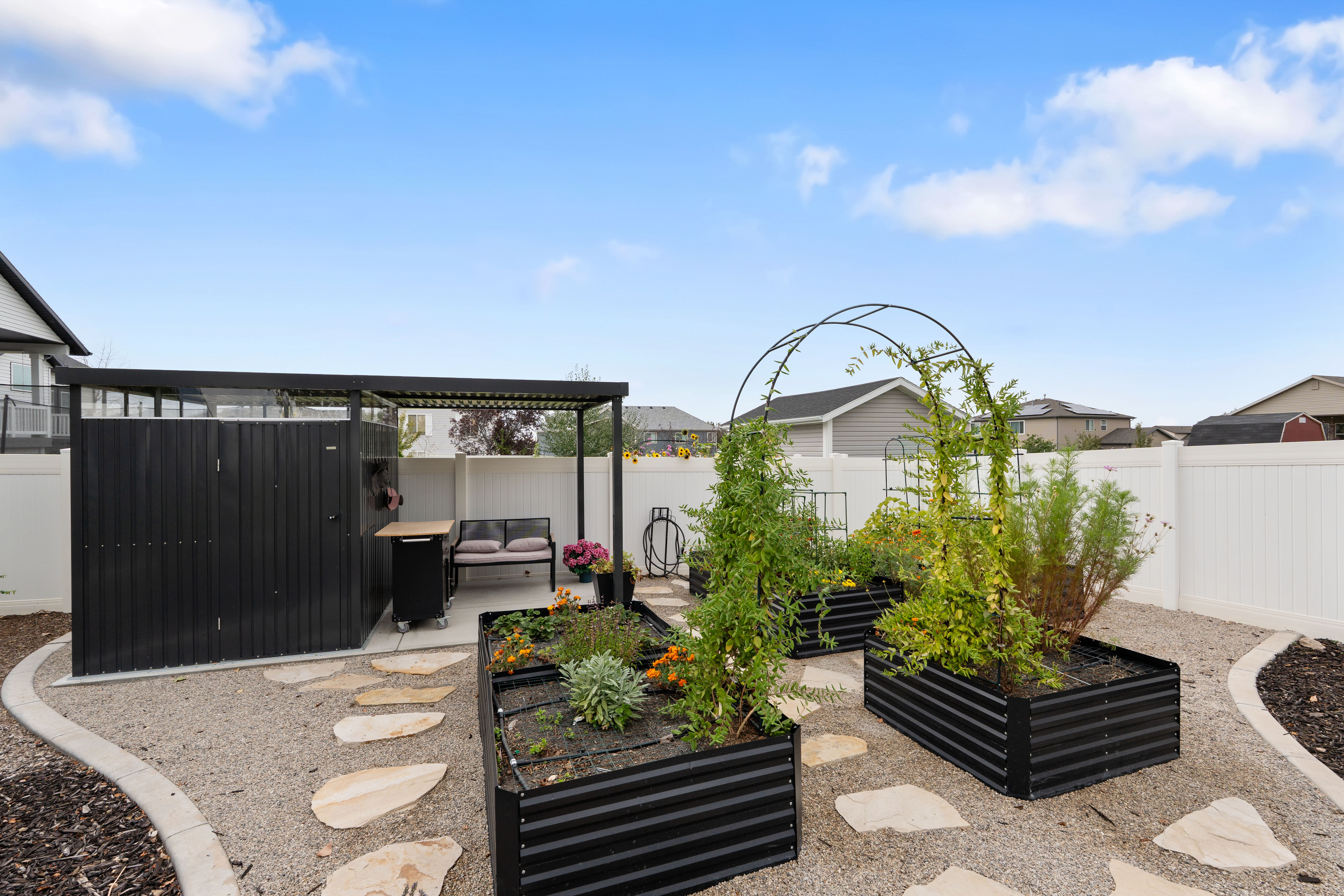 Outdoor space featuring a gravel patio with stepping stones, a black pergola, a storage shed, and multiple raised garden beds