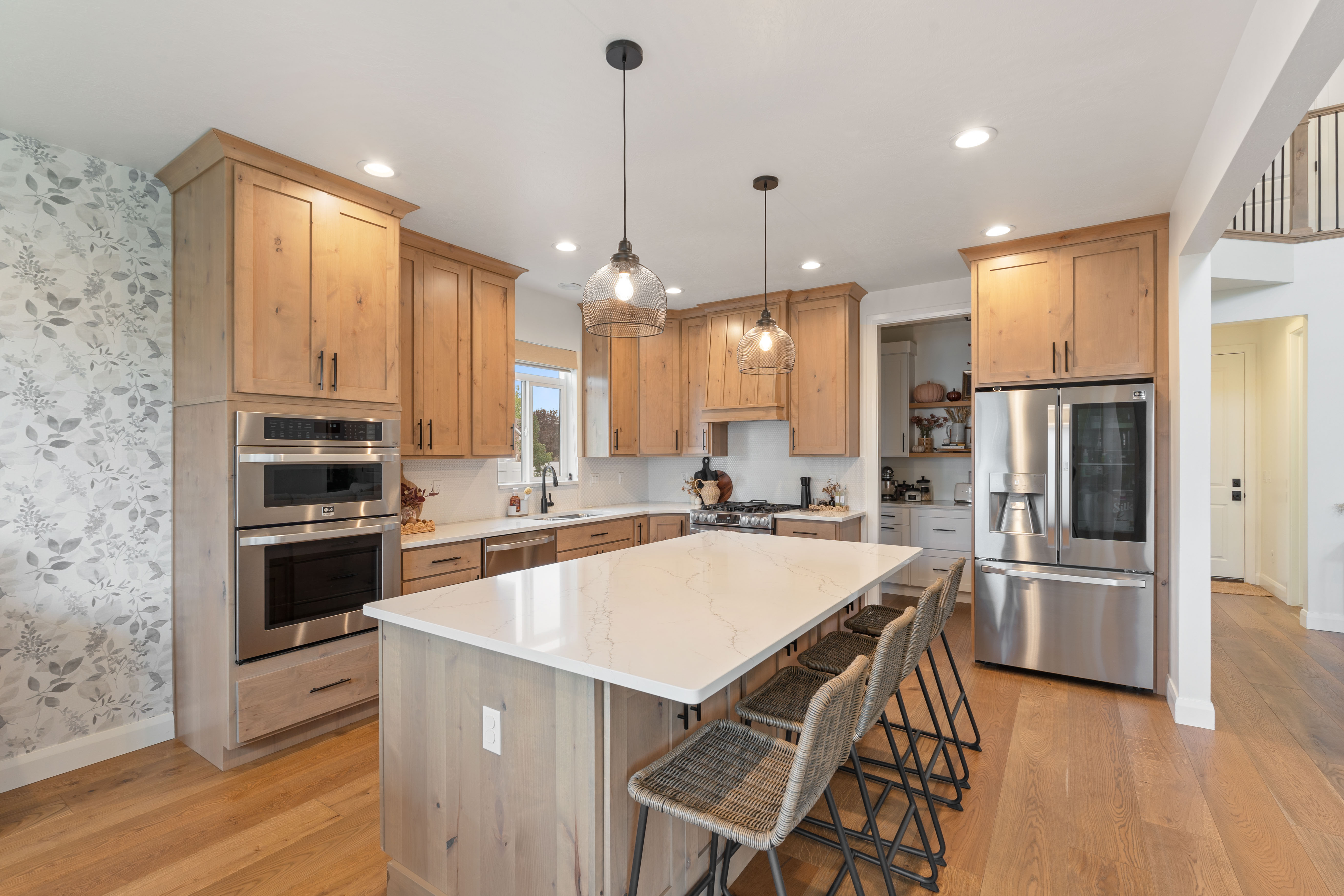 Gourmet kitchen, double ovens, showcasing a large central island with seating, stainless steel appliances, wood-finish cabinetry, recessed lighting, and wood-finish flooring