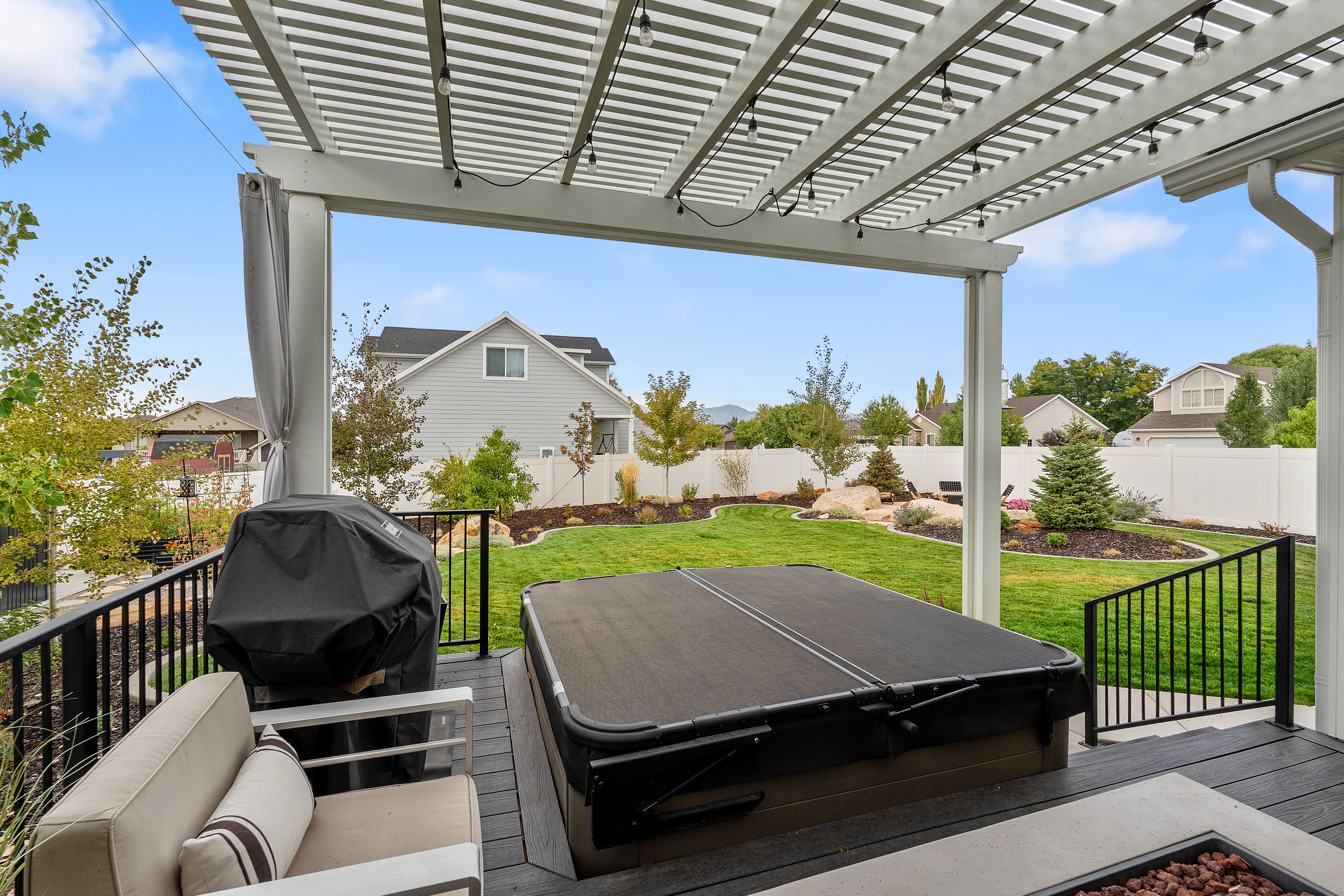 Covered outdoor living space featuring a spa, a fire pit, and a composite deck with black metal railings