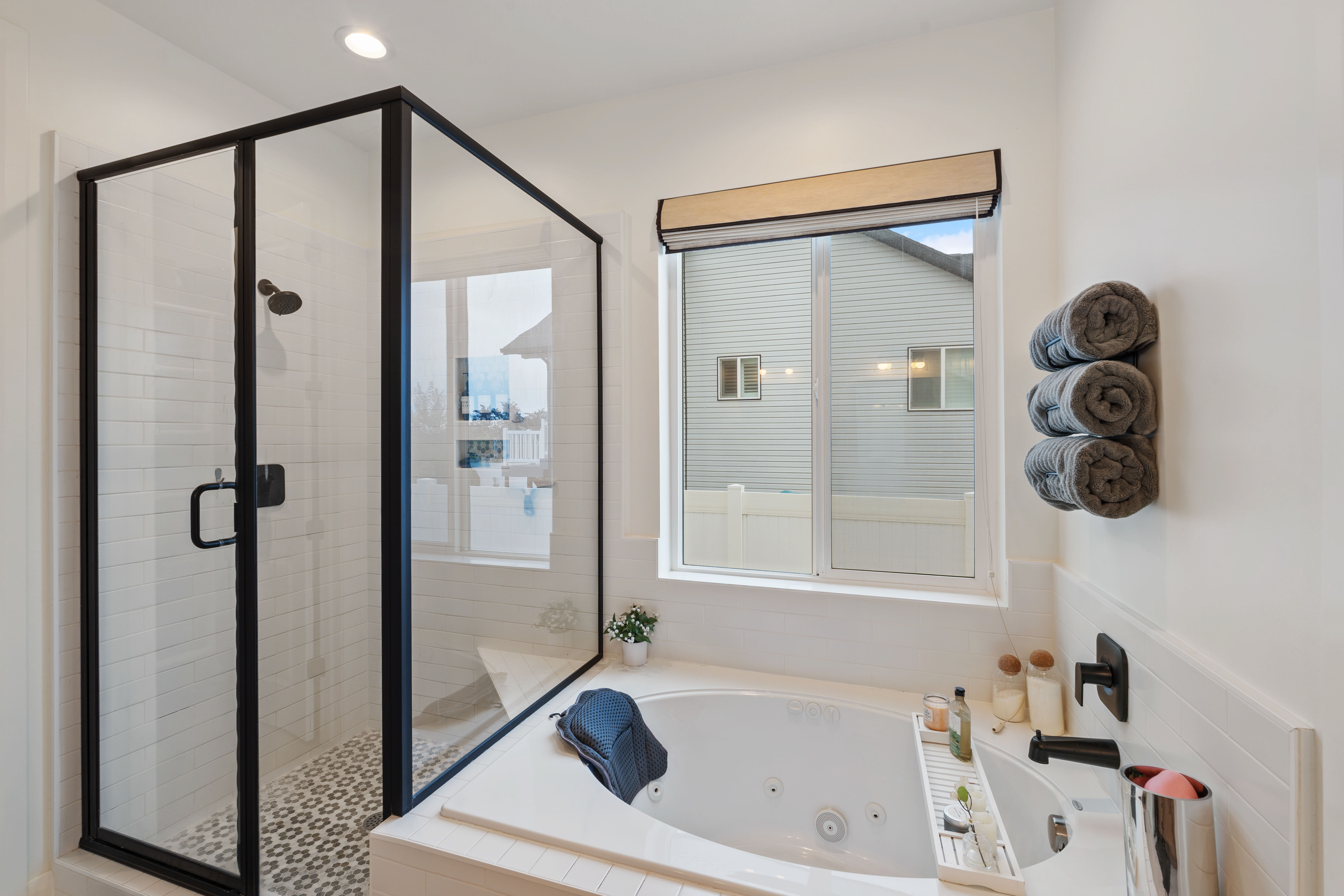 Corner shower with black framed glass enclosure, patterned tile flooring, and a built-in jetted tub