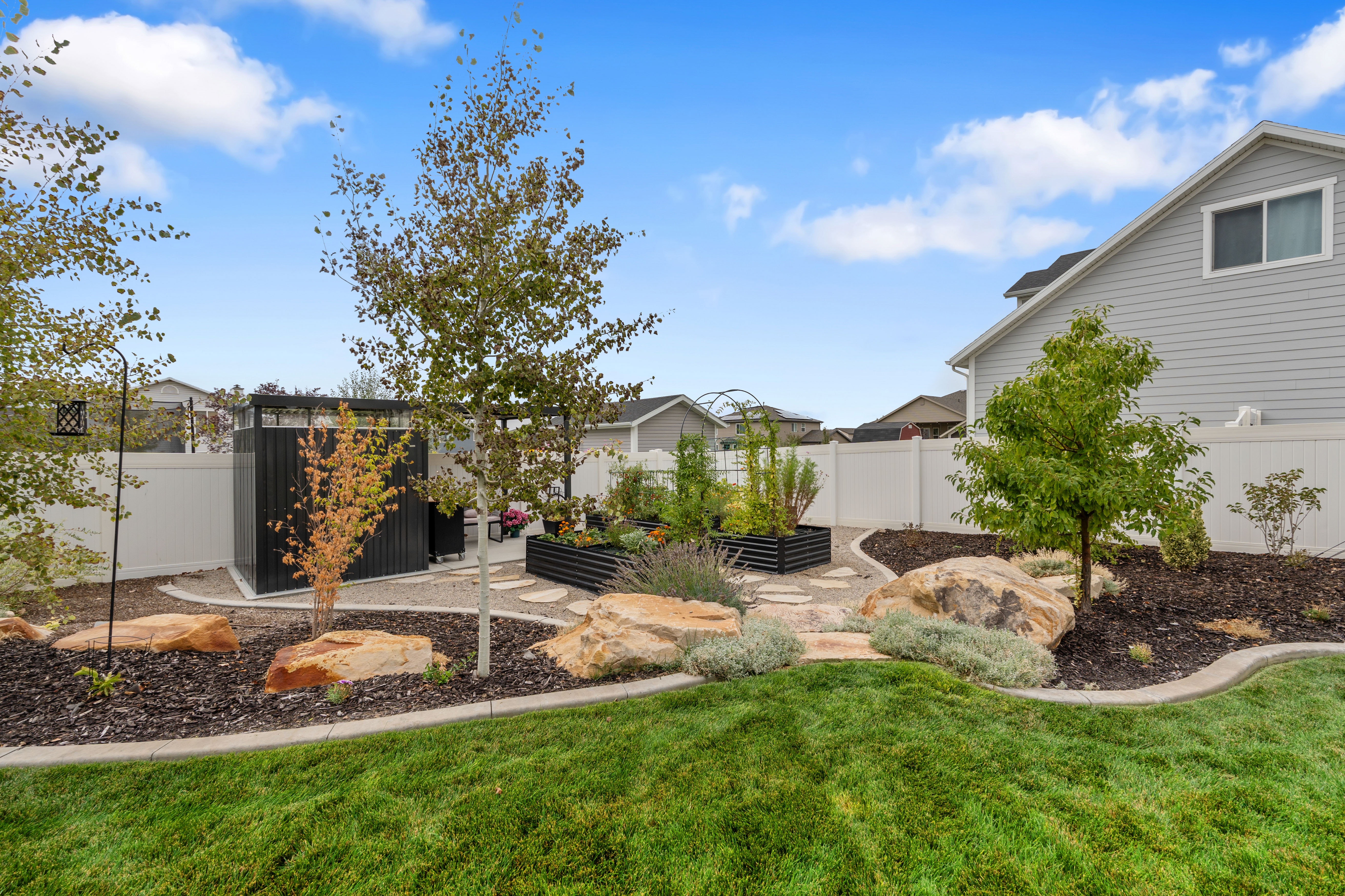 Lush backyard featuring a manicured lawn, established trees, and decorative boulders