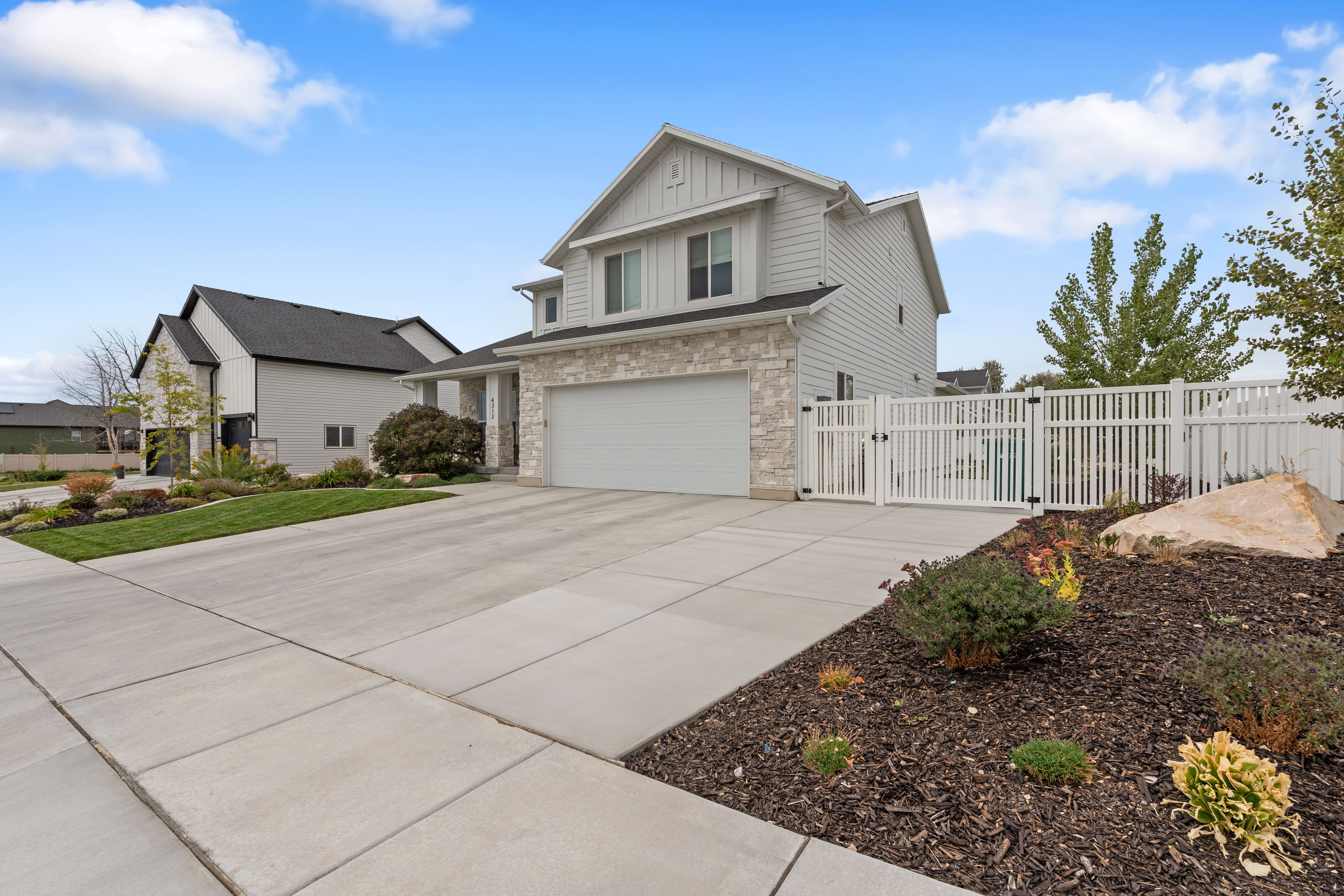 Contemporary two-story residence with a stone and siding facade, featuring a two-car garage, concrete driveway, and a white picket fence