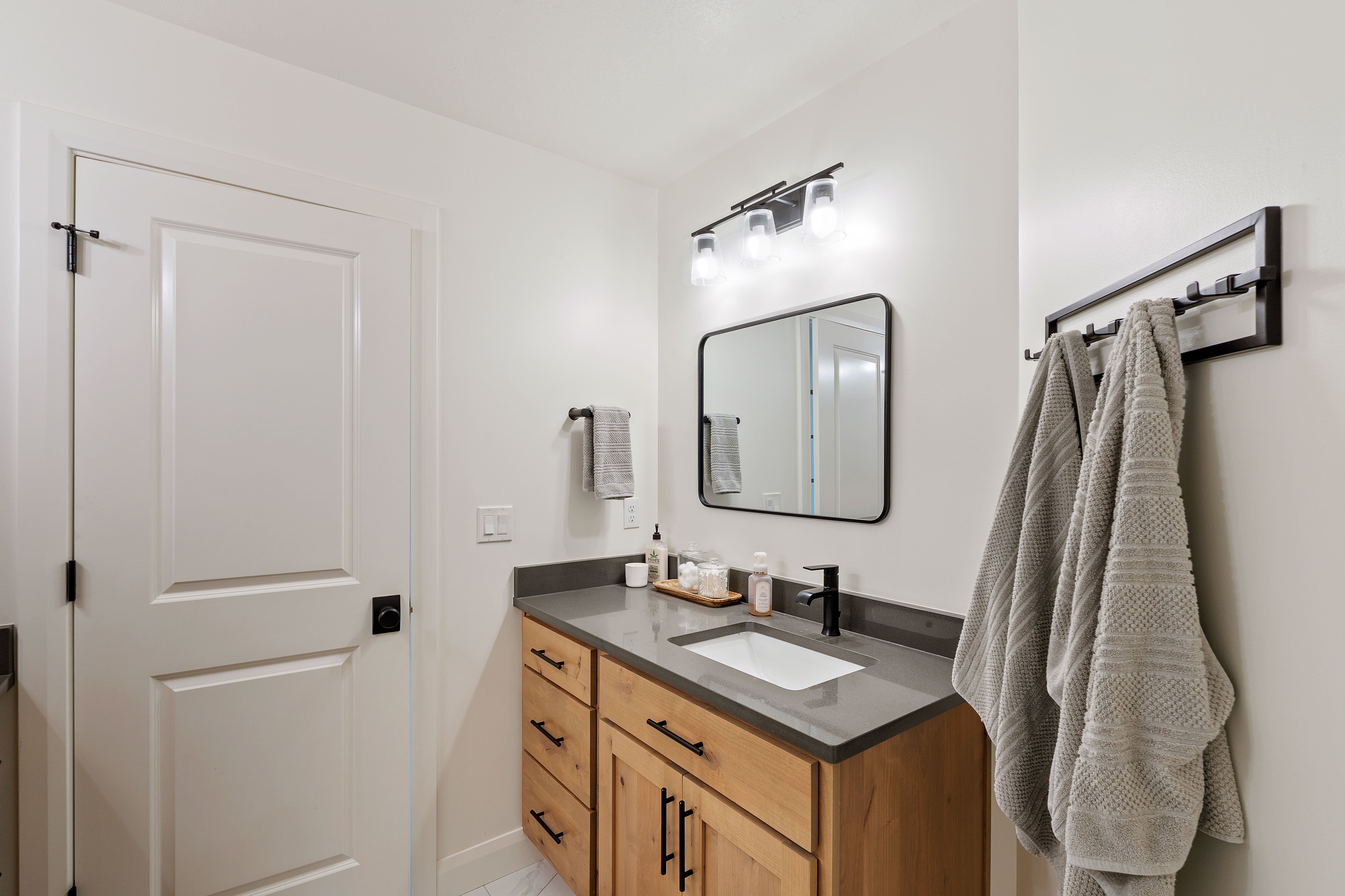 Bathroom vanity featuring a light wood-finish cabinet with black hardware, a rectangular undermount sink, and a gray countertop