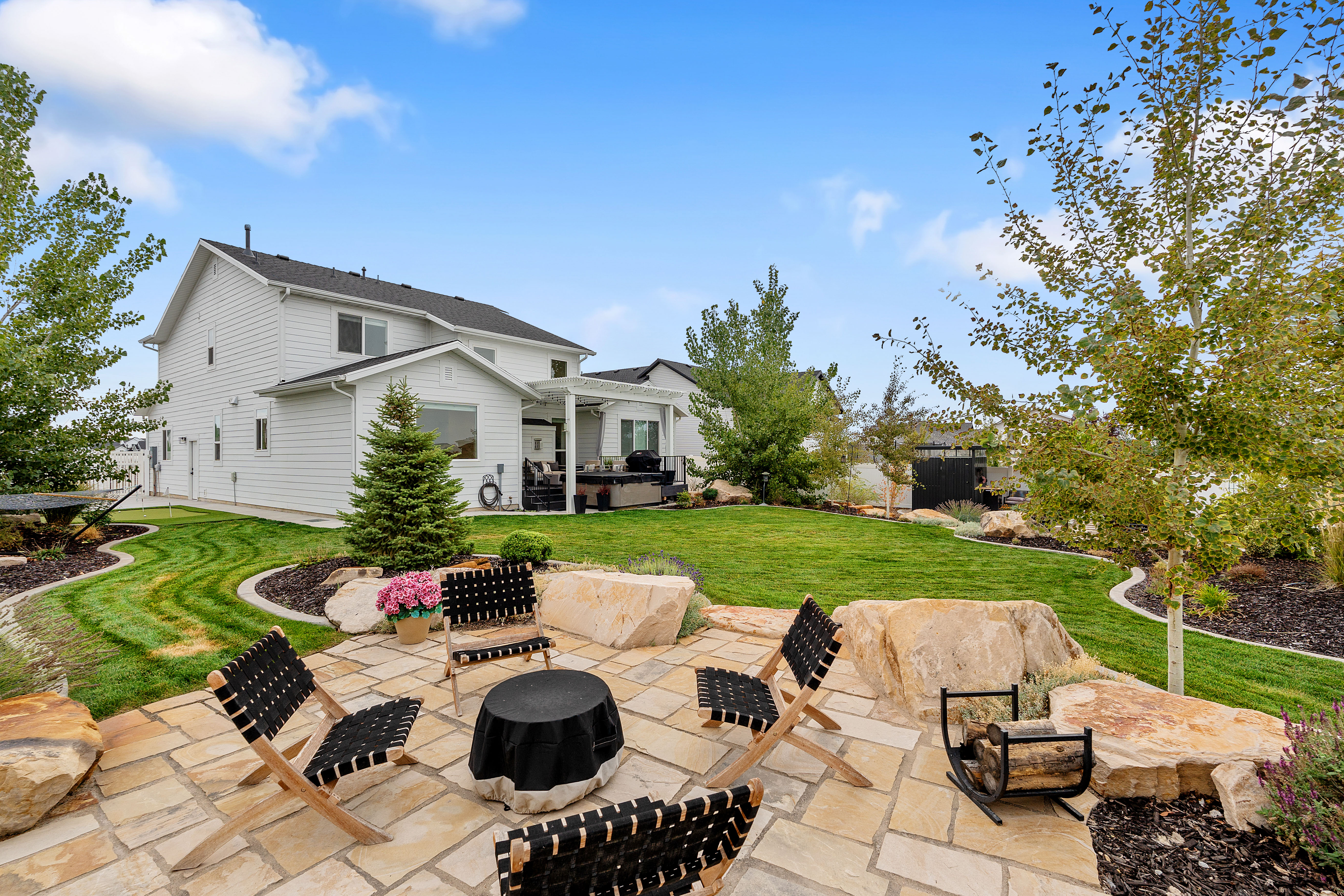 Outdoor Firepit - Expansive backyard featuring a natural stone patio, integrated rock landscaping, manicured lawn, and mature trees