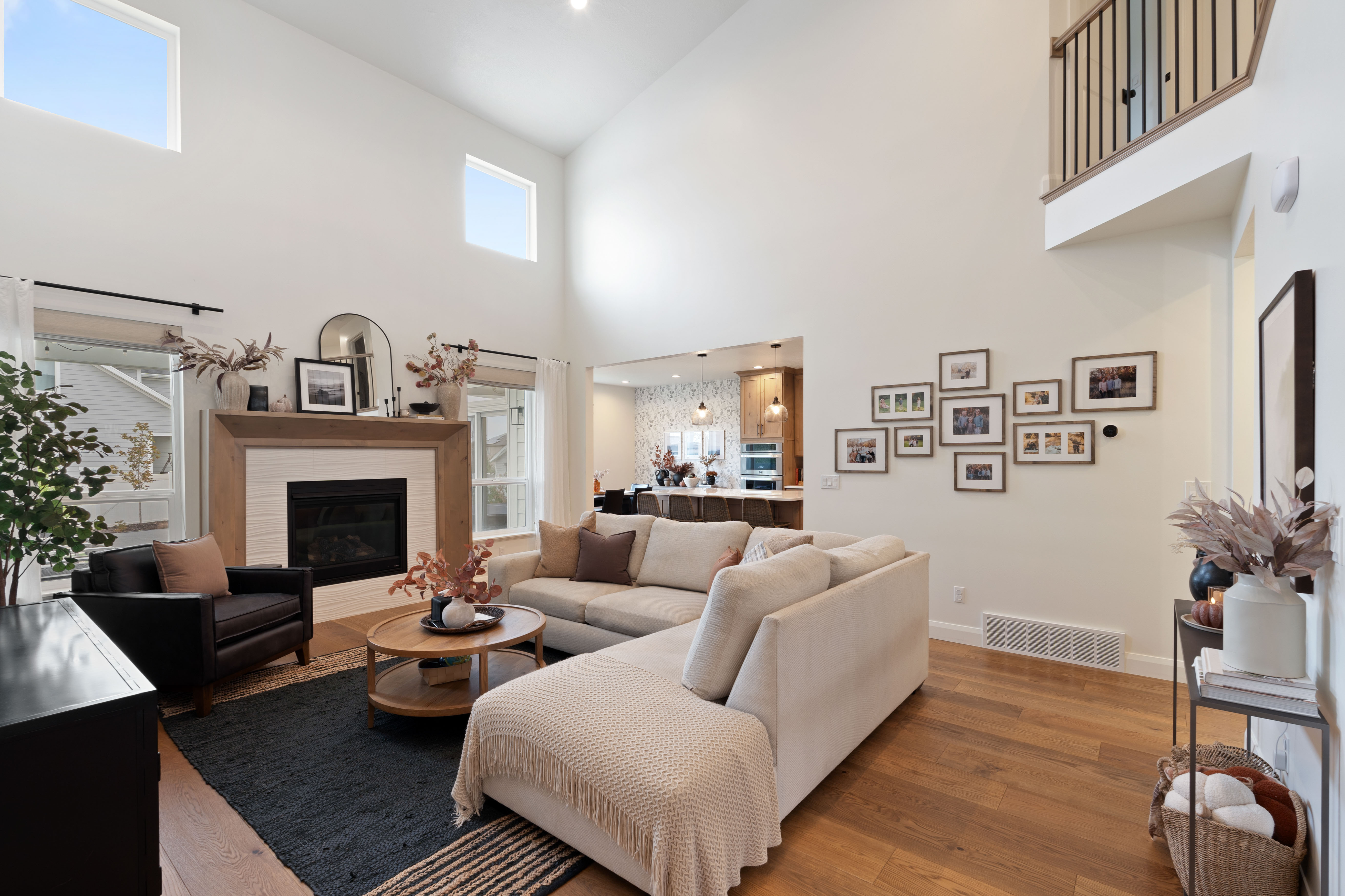 Spacious living area featuring high vaulted ceilings, a fireplace with a light-colored tile surround and wood mantel, large windows, and warm wood-finish flooring