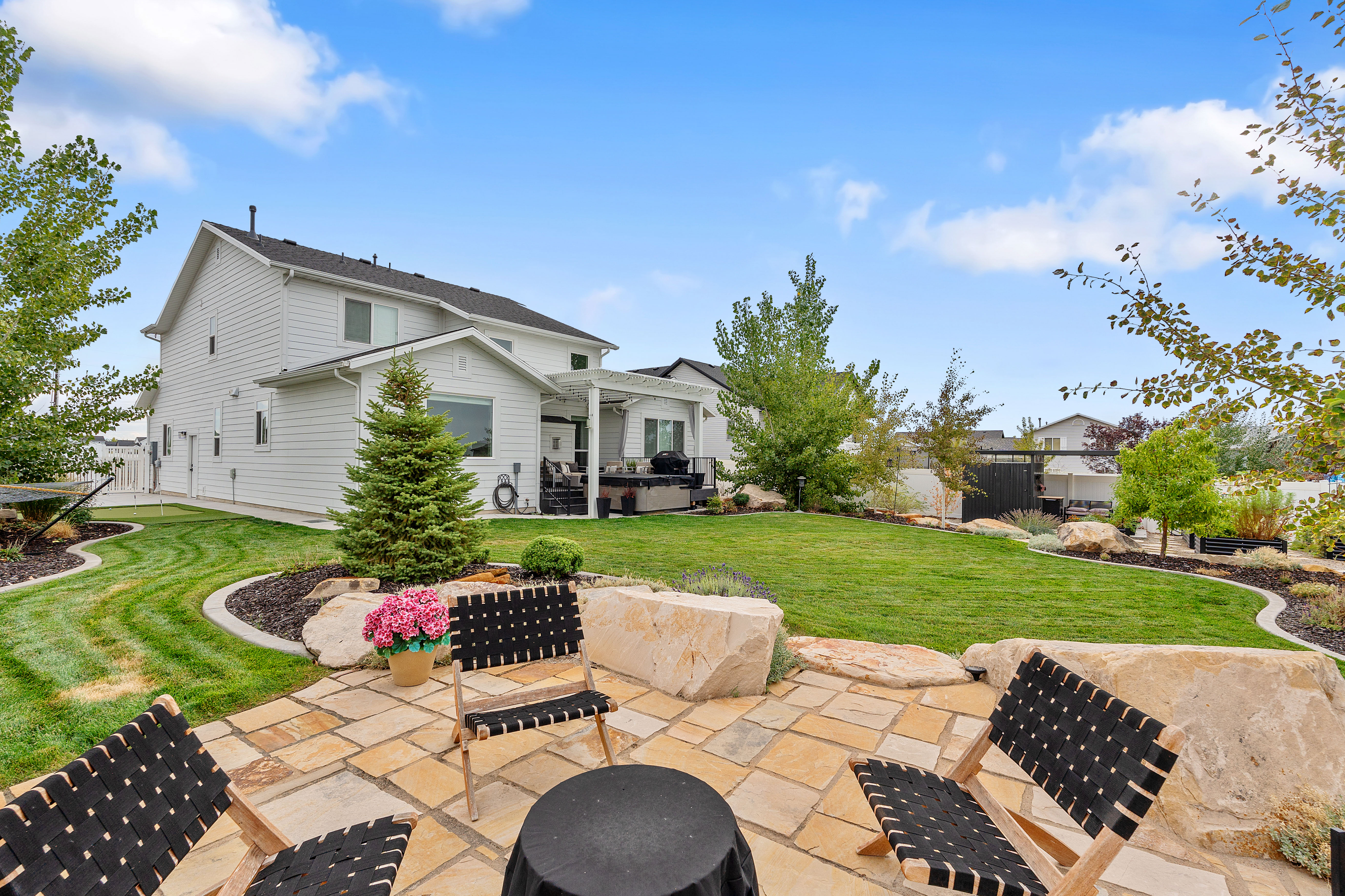 Expansive backyard featuring a stone patio, manicured lawn, and mature landscaping
