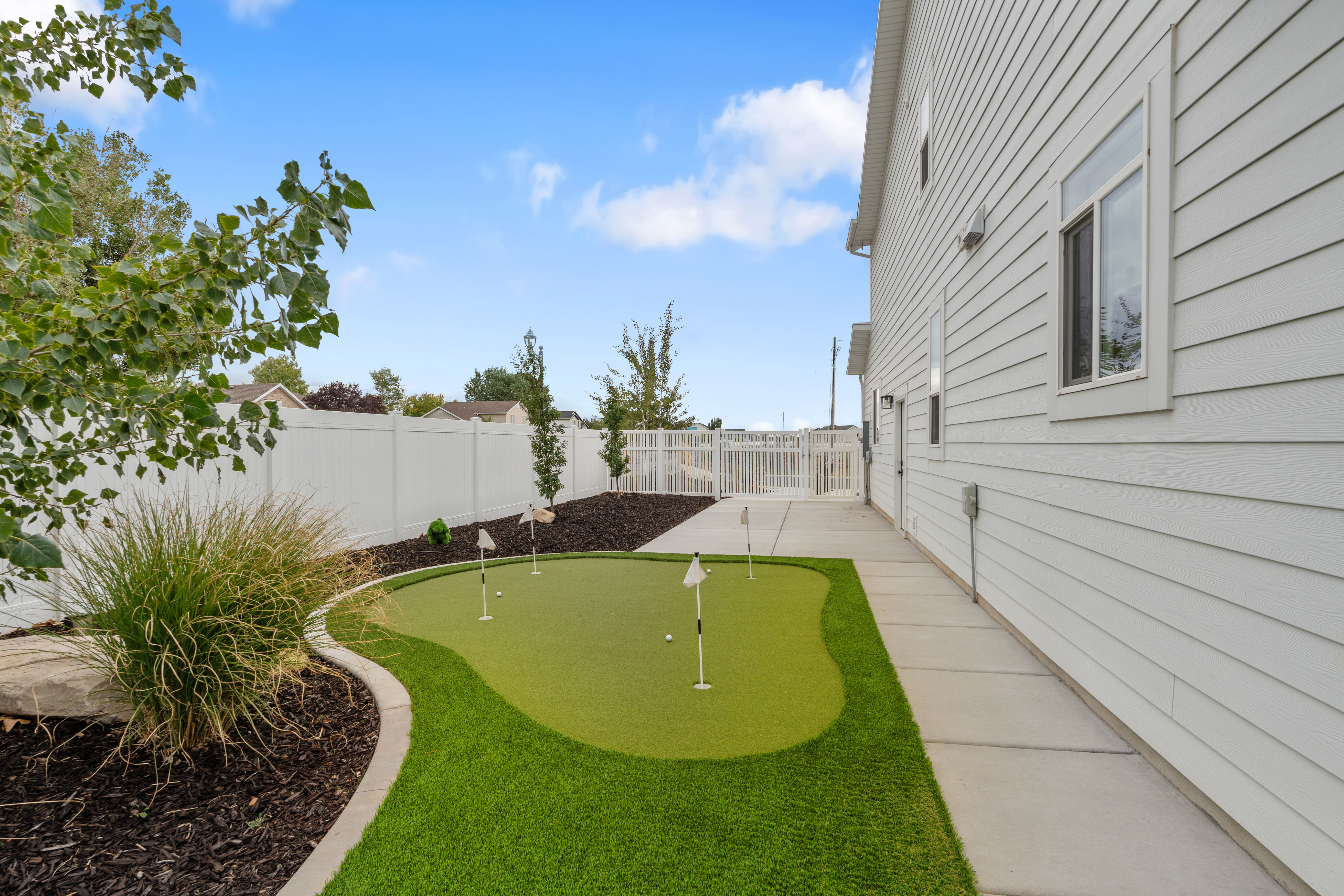 Putting green with multiple holes, bordered by a concrete curb and woodchip landscaping