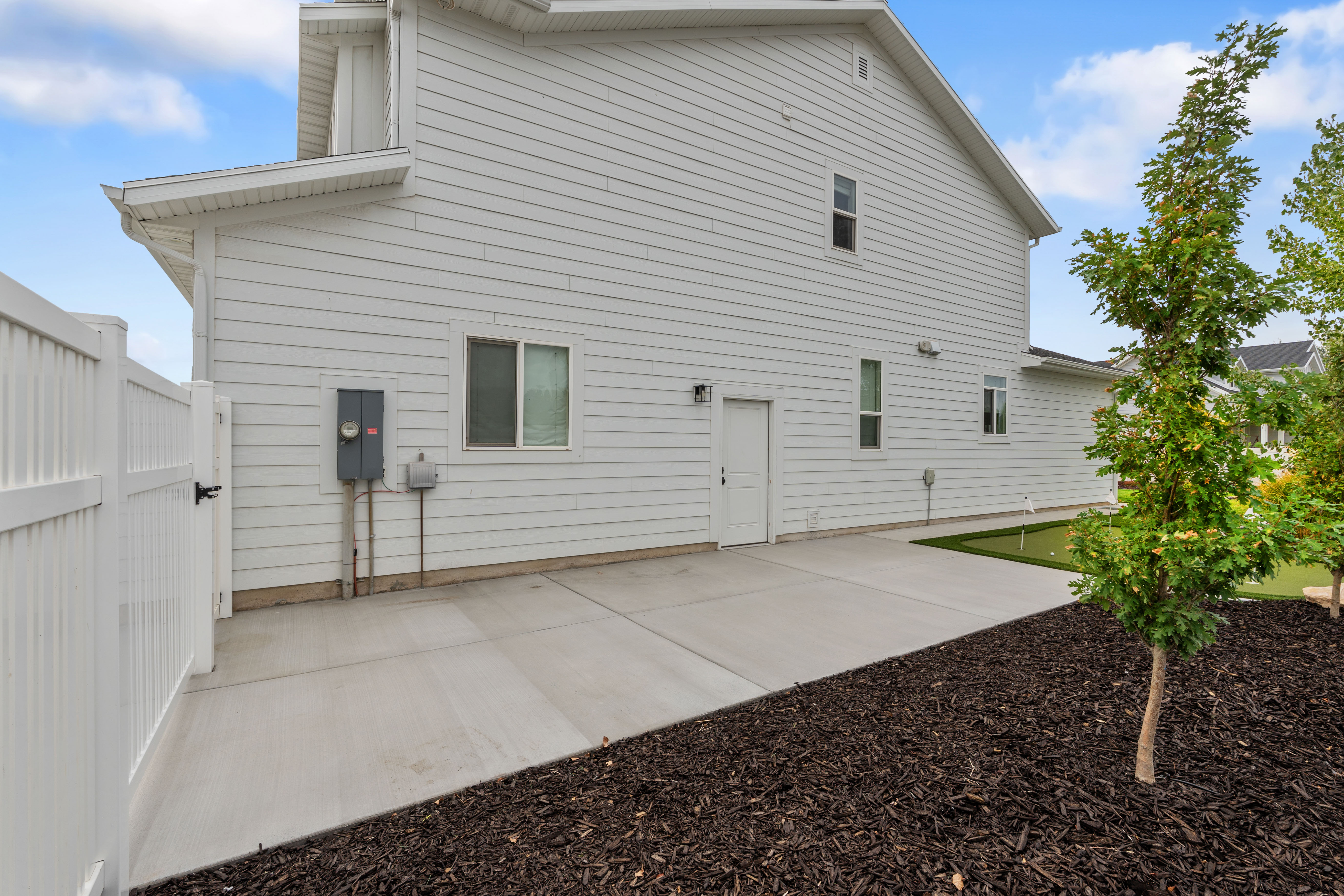 RV parking pad, White vinyl siding exterior with an expansive concrete patio and adjacent mulched landscaping