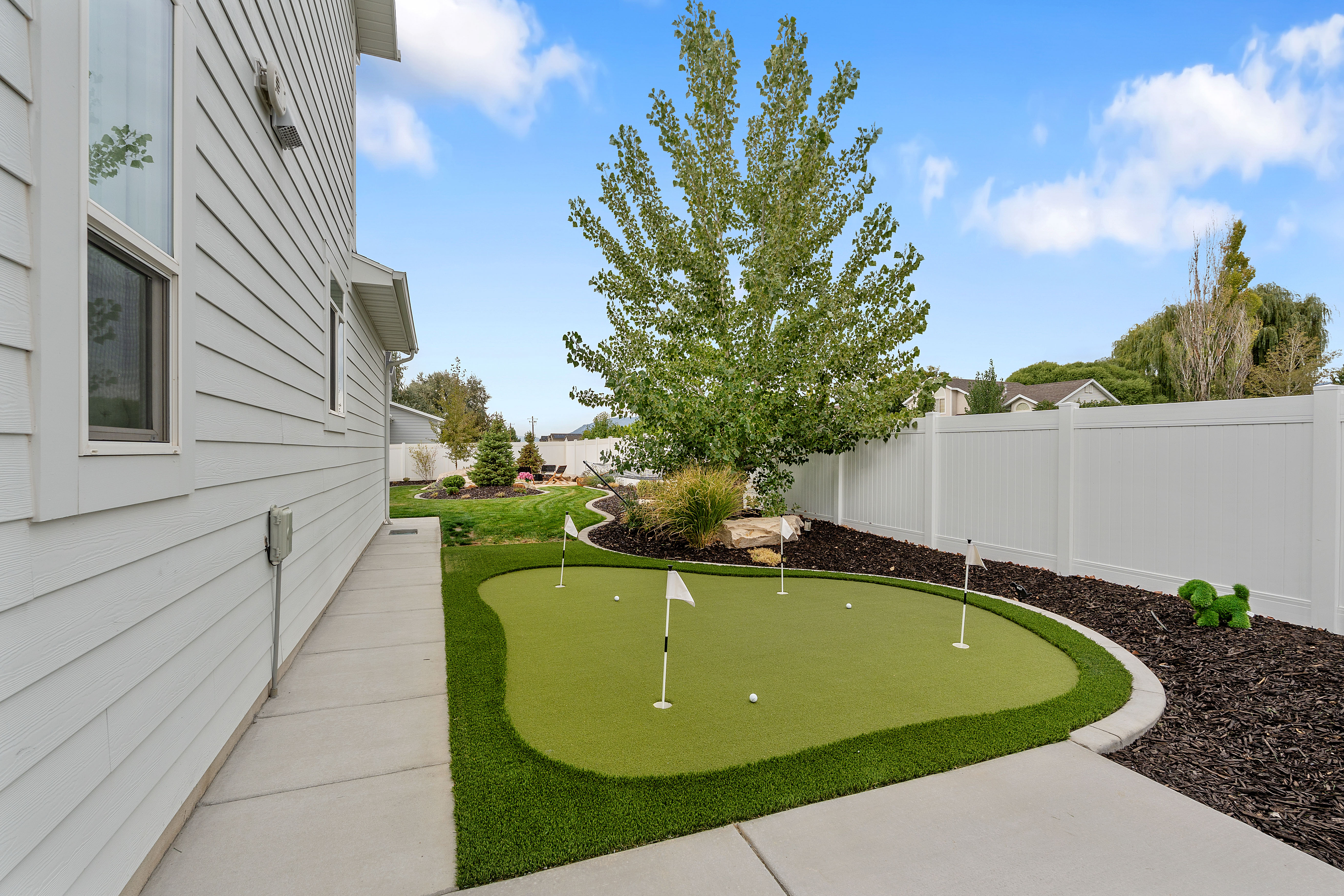 Backyard featuring a dedicated putting green with multiple holes, a privacy fence, and mature landscaping