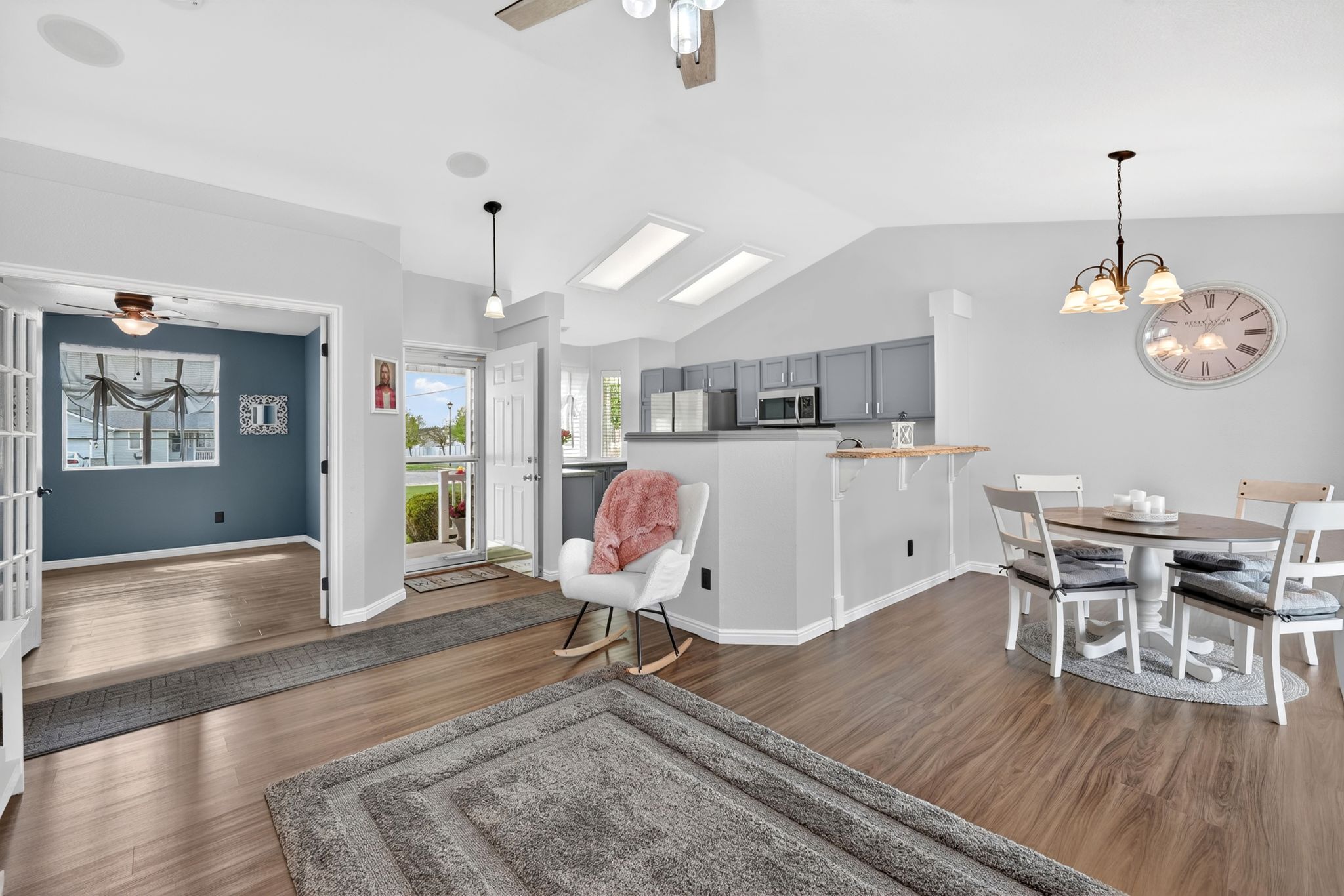 Spacious open-concept living area featuring wood-finish flooring, vaulted ceilings, and skylights