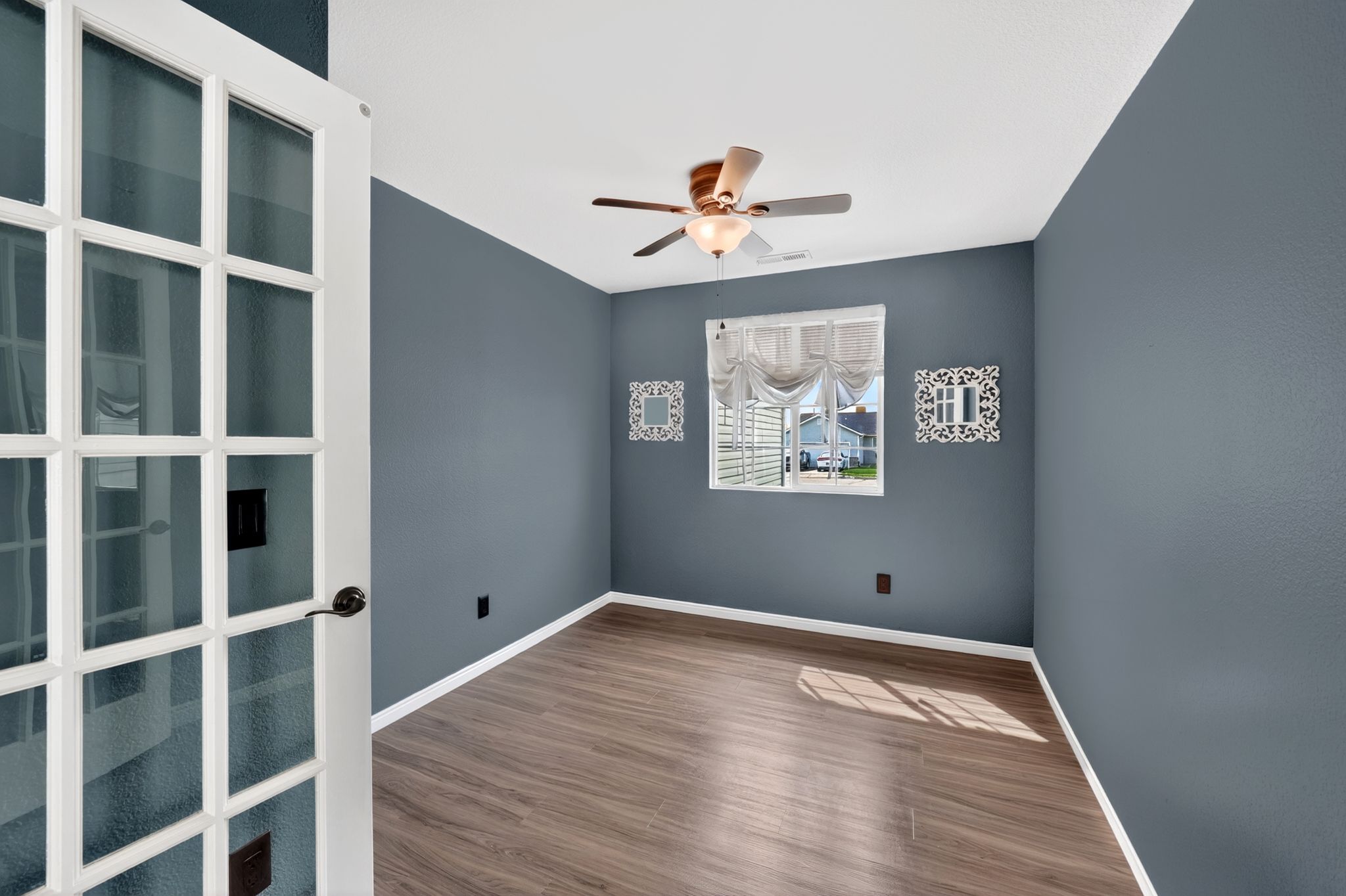 French doors open to a versatile room featuring wood-finish flooring, a ceiling fan with light fixture, and a window with blinds