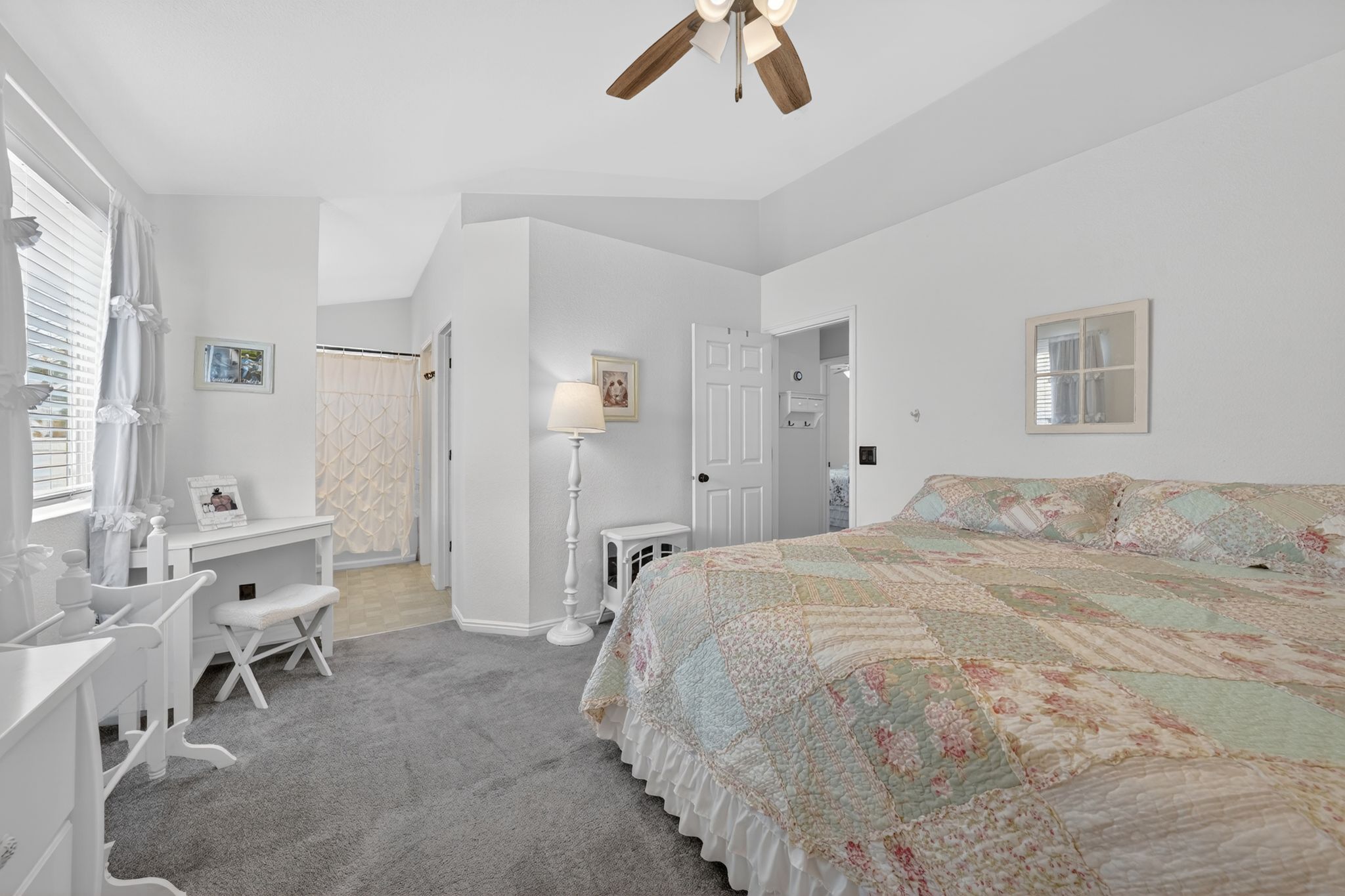 Spacious bedroom featuring vaulted ceilings, a ceiling fan with light fixture, gray carpeting, and a window with blinds