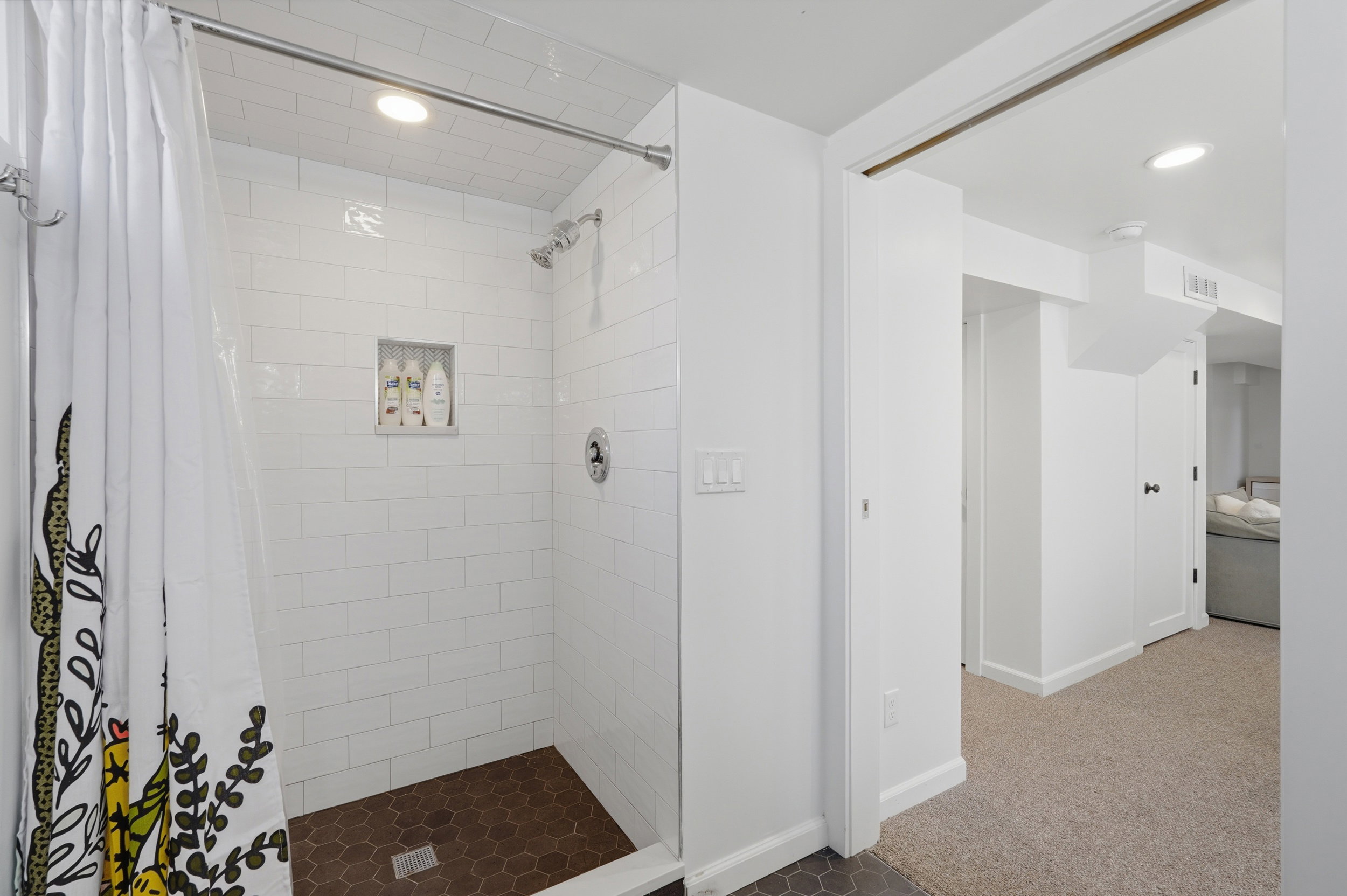 Shower stall featuring white subway tile surround, dark hexagonal floor tiling, and a recessed niche
