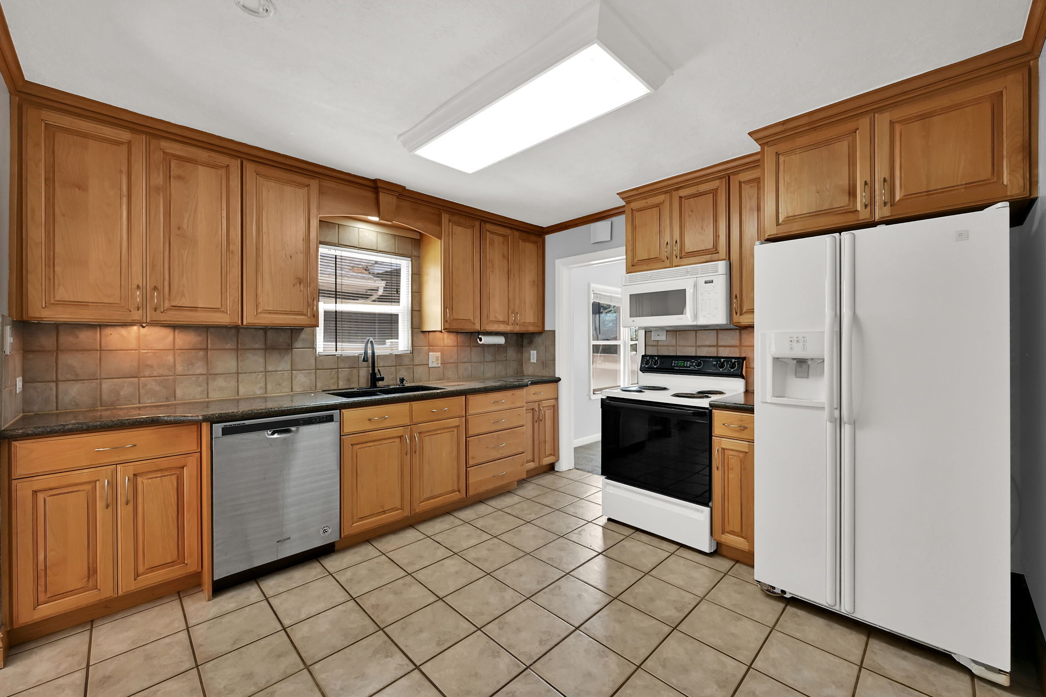 Kitchen with wood cabinetry, dark countertops, and a tiled backsplash