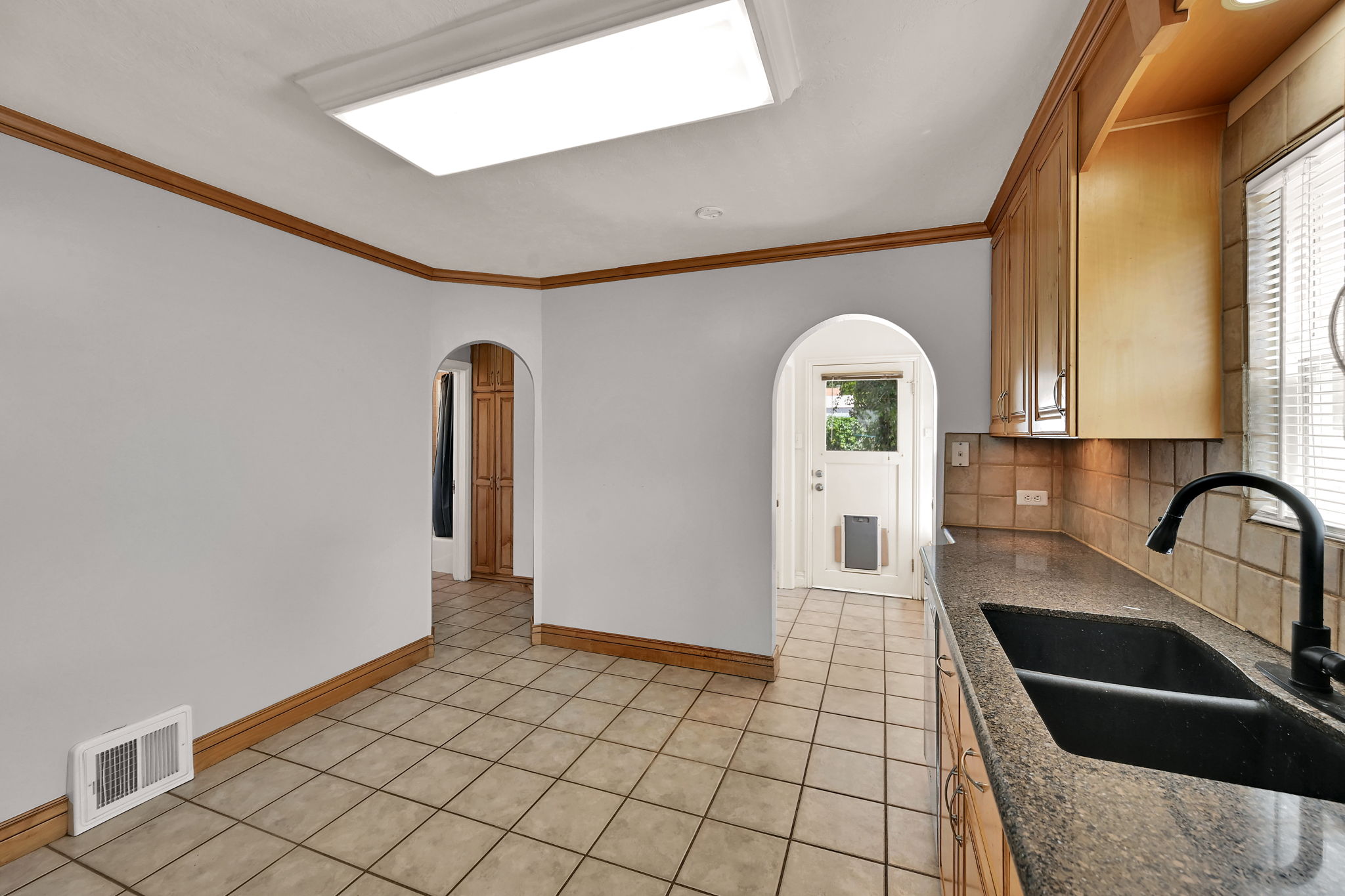 Kitchen area featuring light-toned tile flooring, light wood cabinetry, and dark countertop with a double basin sink