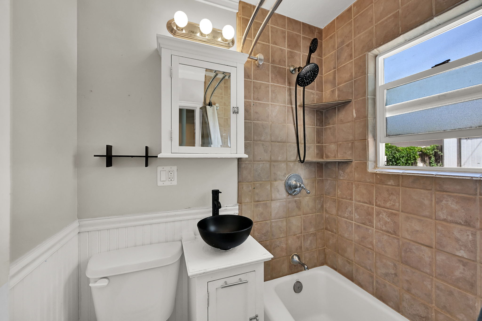Bathroom featuring a white vanity with a black vessel sink, a white medicine cabinet with integrated lighting, and a bathtub with tile surround