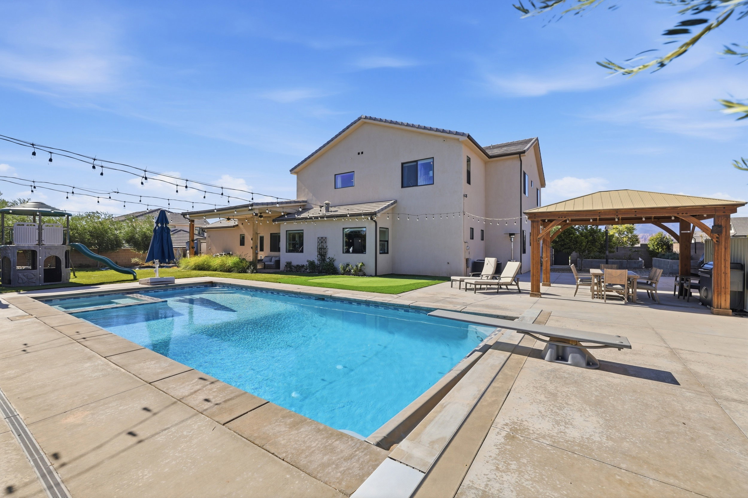 Expansive backyard featuring a large swimming pool with concrete decking, a diving board, and an adjacent covered patio area