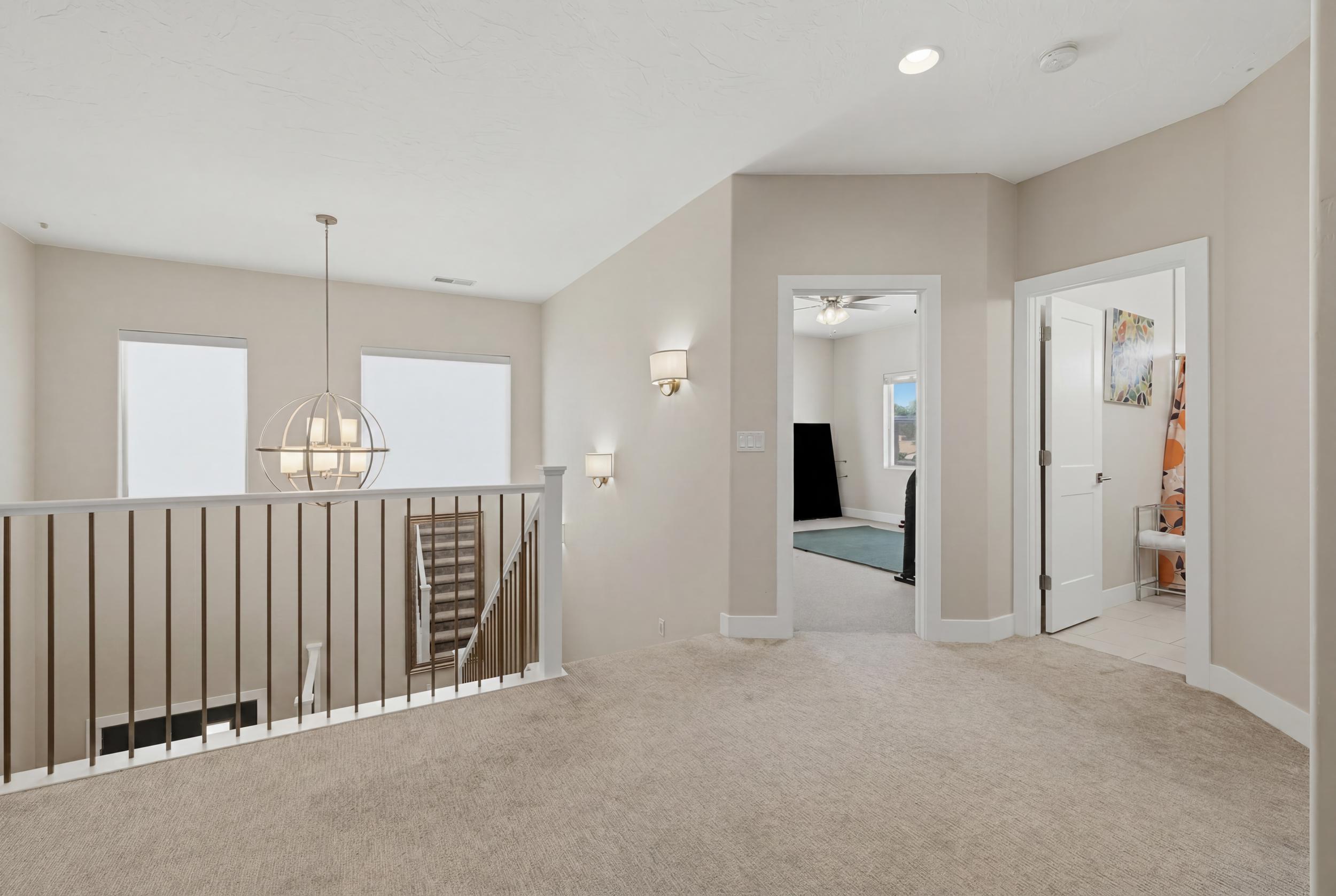 Upper-level hallway featuring neutral carpeting, a contemporary chandelier, two wall sconces, and multiple doorways leading to additional rooms