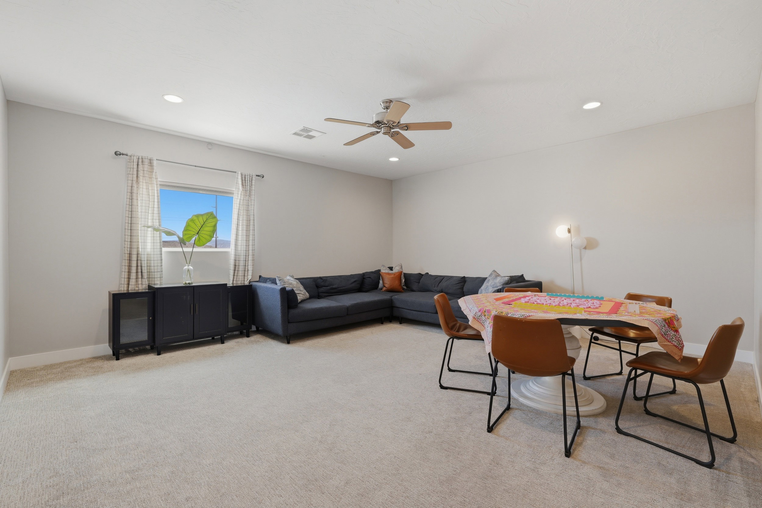 Spacious carpeted room featuring a window with patterned drapes, recessed lighting, and a ceiling fan