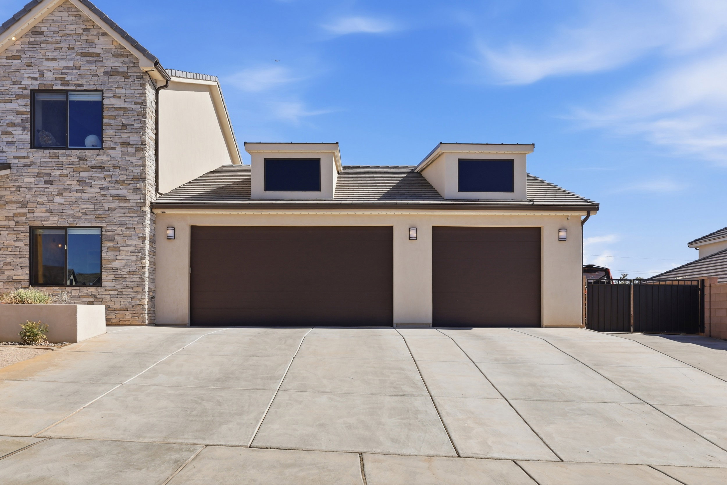 Exterior with stacked stone facade and stucco finish, featuring a concrete driveway, two brown garage doors, and two dormer windows