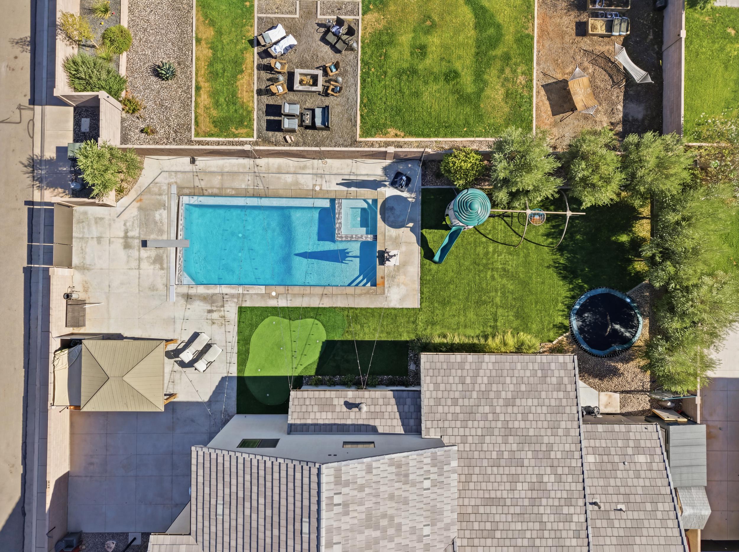 Expansive backyard featuring a rectangular swimming pool with diving board, a separate turf putting green, and a large grass lawn