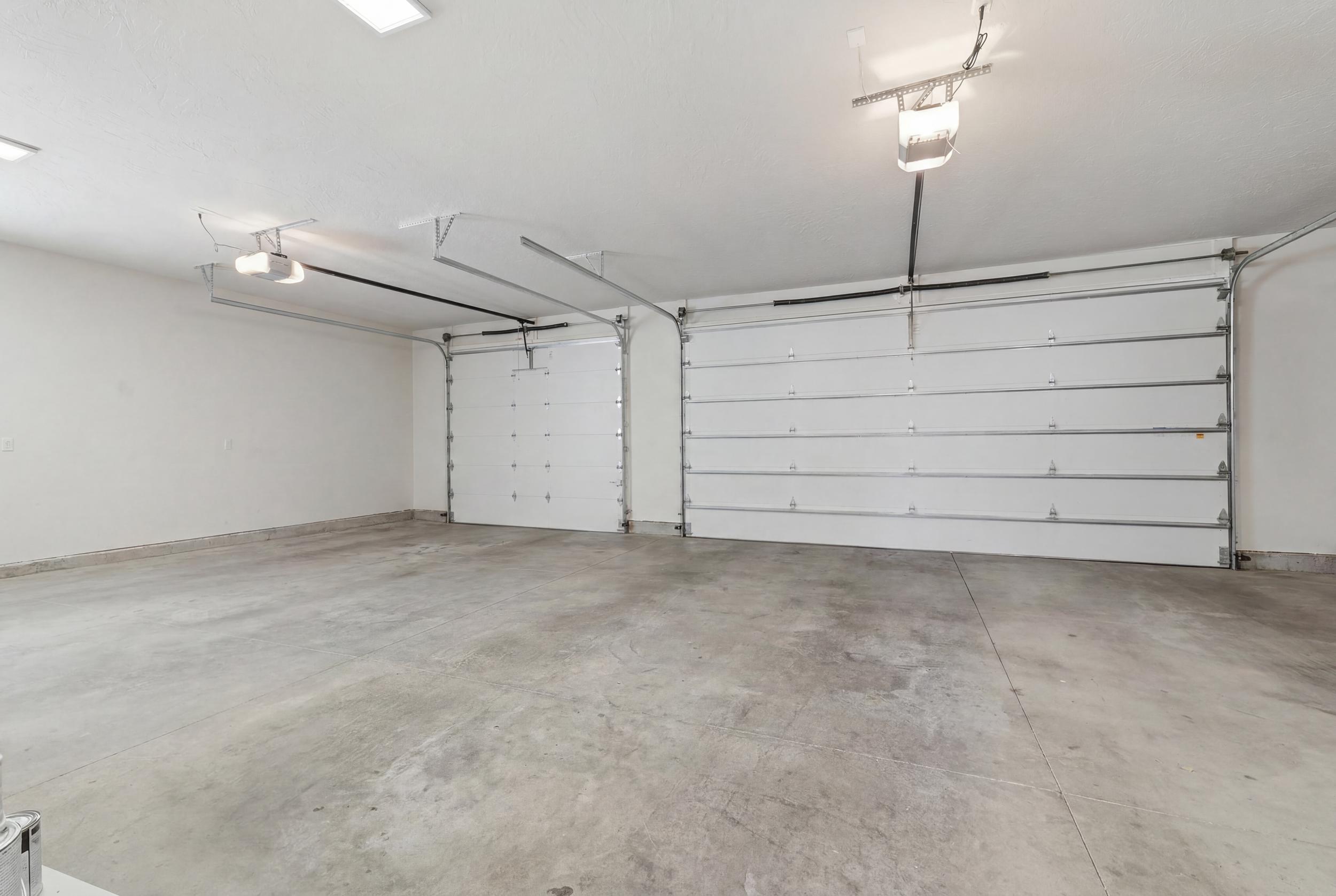 Spacious garage featuring a concrete floor, two white overhead doors with openers, and overhead lighting