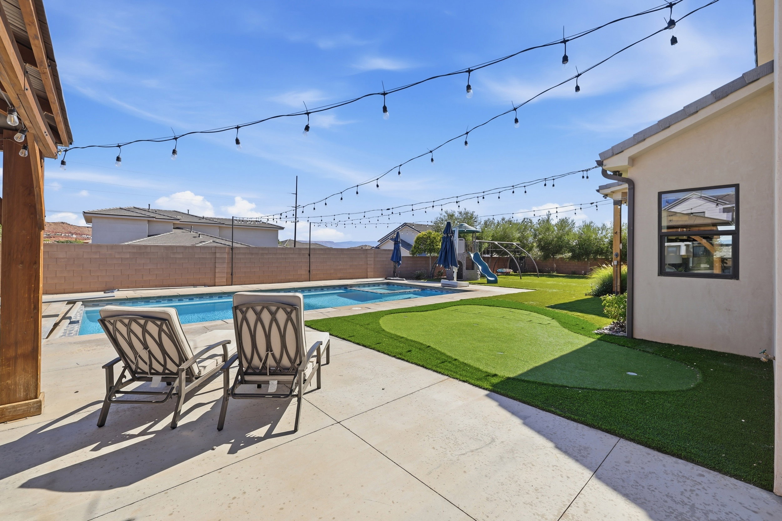 Expansive backyard oasis featuring a rectangular swimming pool, concrete patio, and putting green