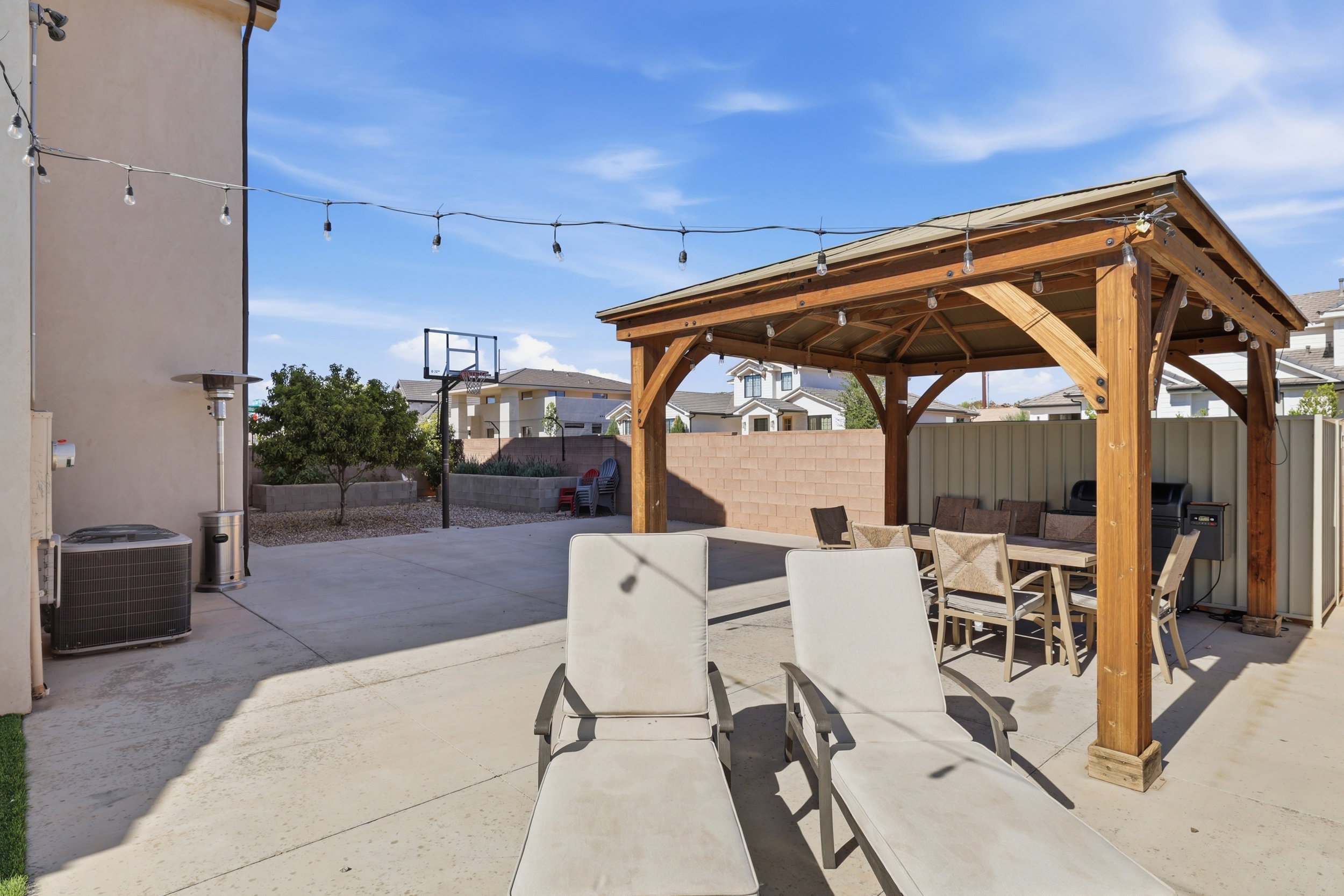 Expansive concrete patio featuring a large wooden gazebo, string lighting, and a basketball hoop
