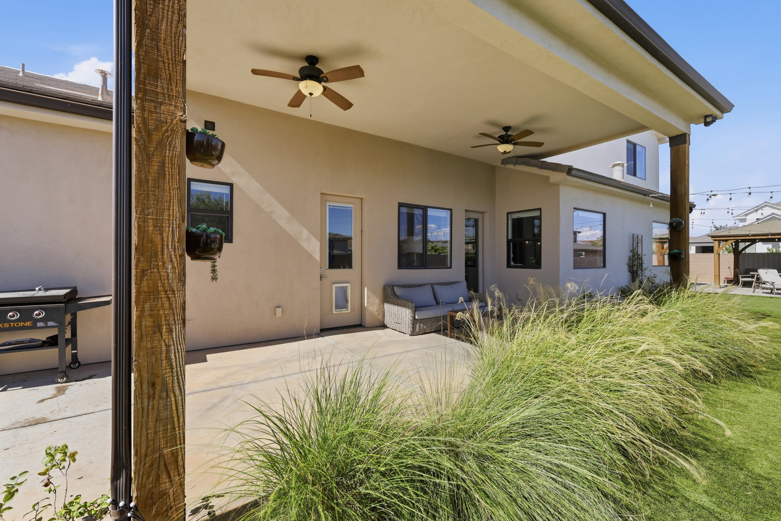 Covered concrete patio with two ceiling fans, surrounded by mature ornamental grasses and a manicured lawn