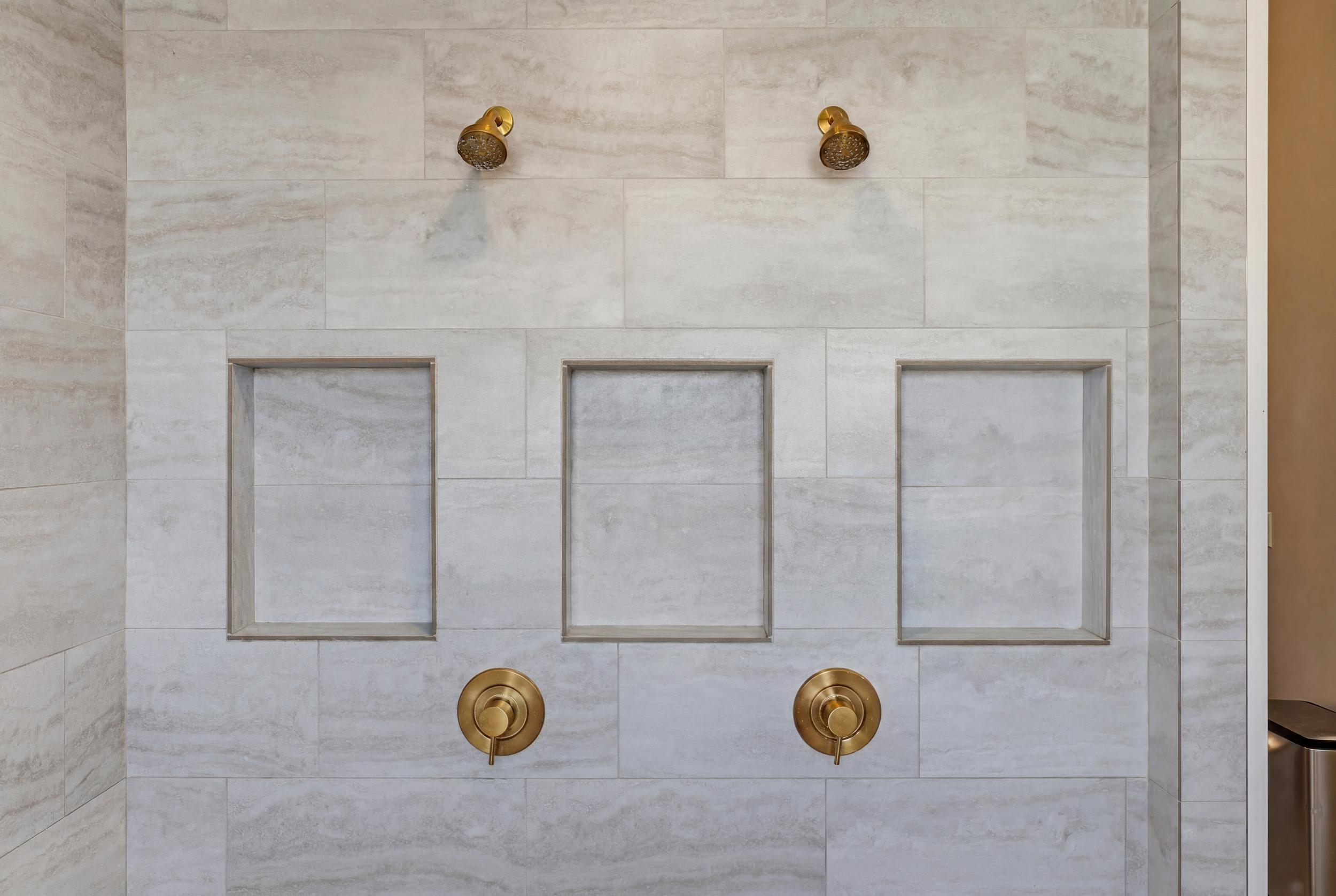 Shower surround featuring large-format tile, dual shower heads, and three recessed niches