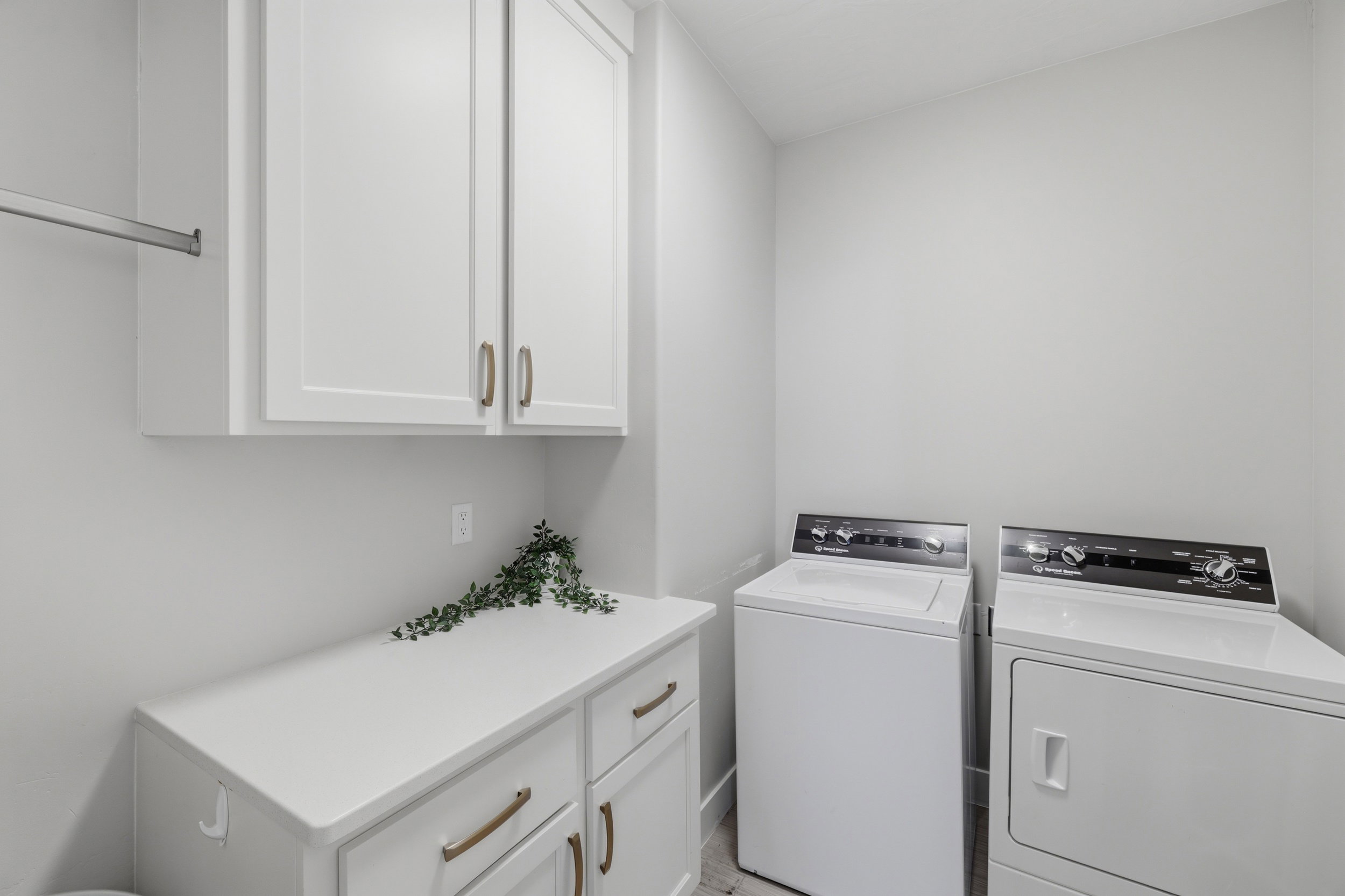 Dedicated laundry area featuring white shaker-style cabinetry with bronze hardware, a white countertop, and a metal hanging rod