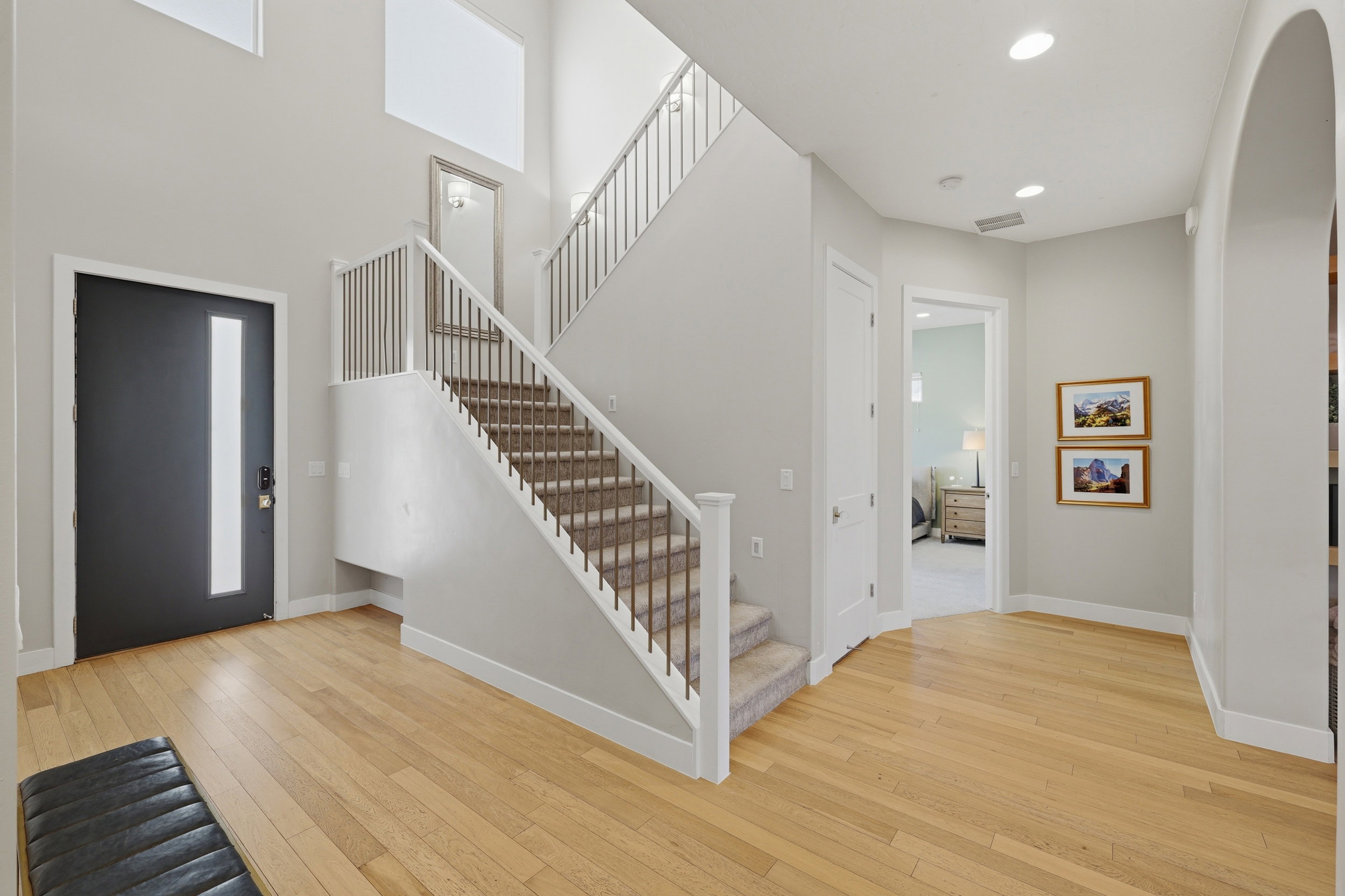 Two-story entryway featuring light wood-finish flooring, a contemporary dark entry door with vertical glass insert, a staircase with white balusters and carpeted treads, and high ceilings with upper-level windows