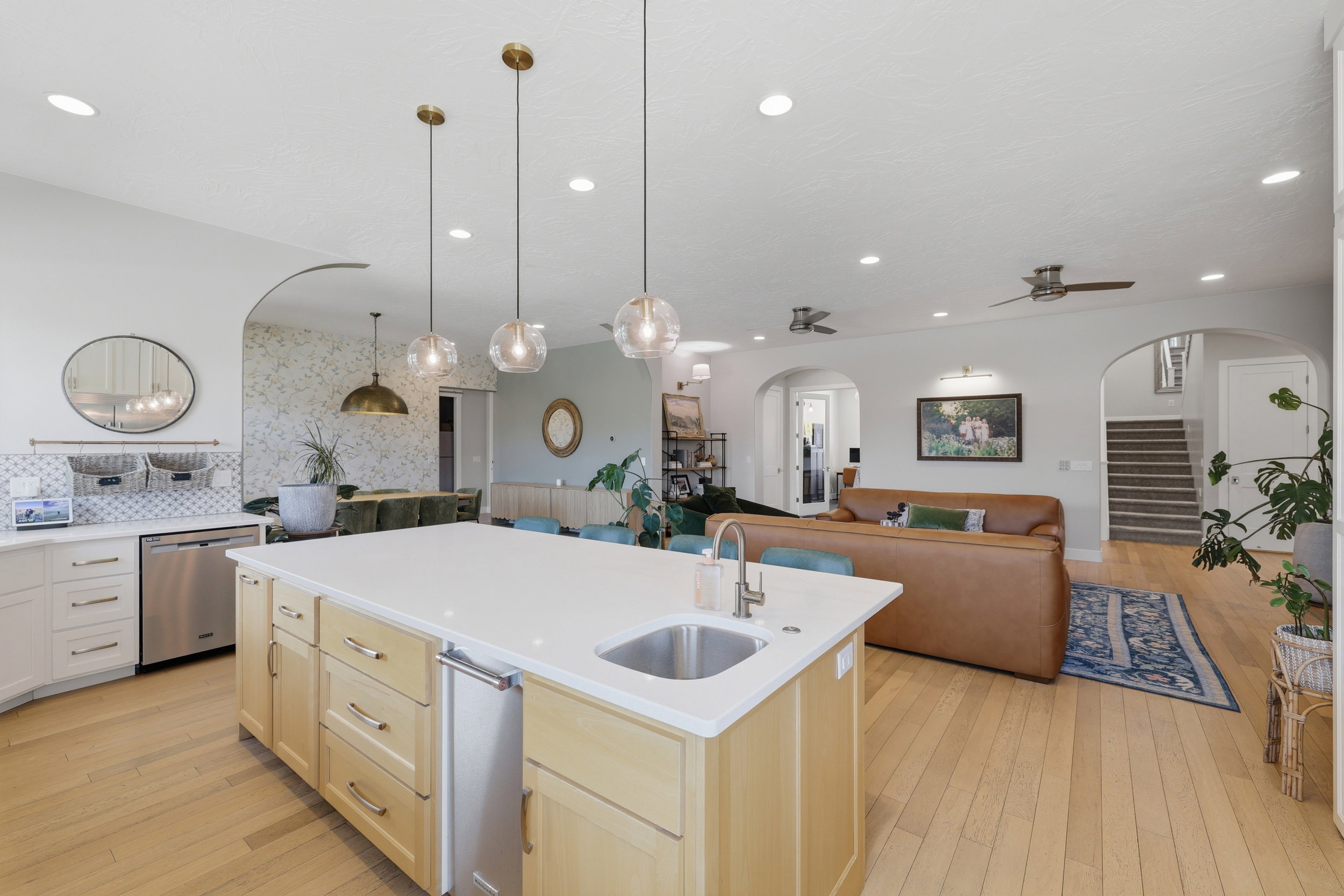 Kitchen island with an undermount sink, integrated mini-refrigerator, and three pendant lights over a light-toned wood-finish floor