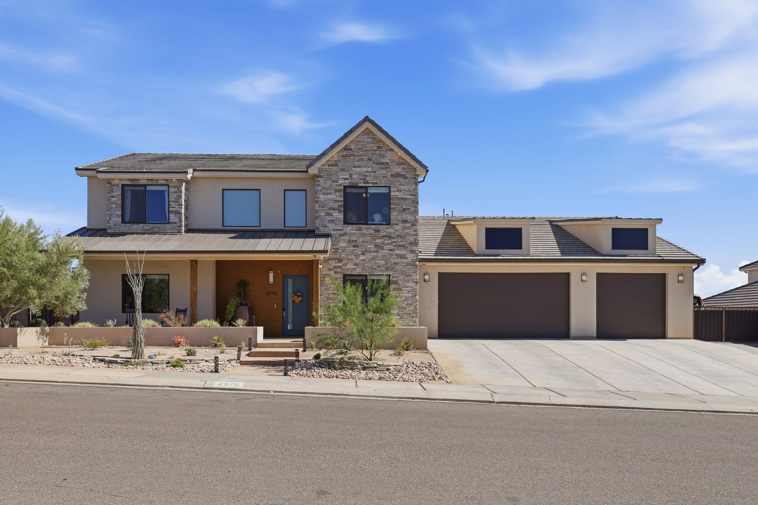 Contemporary two-story residence featuring a stone and stucco exterior, a covered front entry with wood paneling, a dark blue front door, and a two-car garage