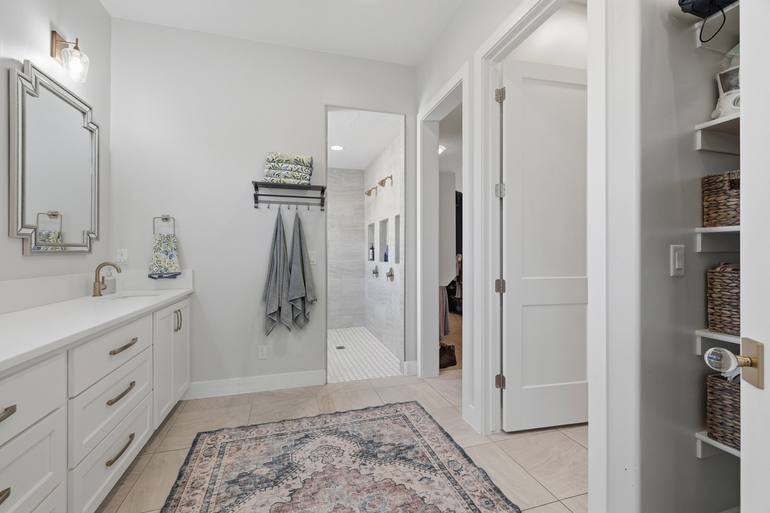 Modern bathroom featuring a single vanity with a white countertop and bronze hardware, framed mirror, and a tiled walk-in shower with multiple showerheads