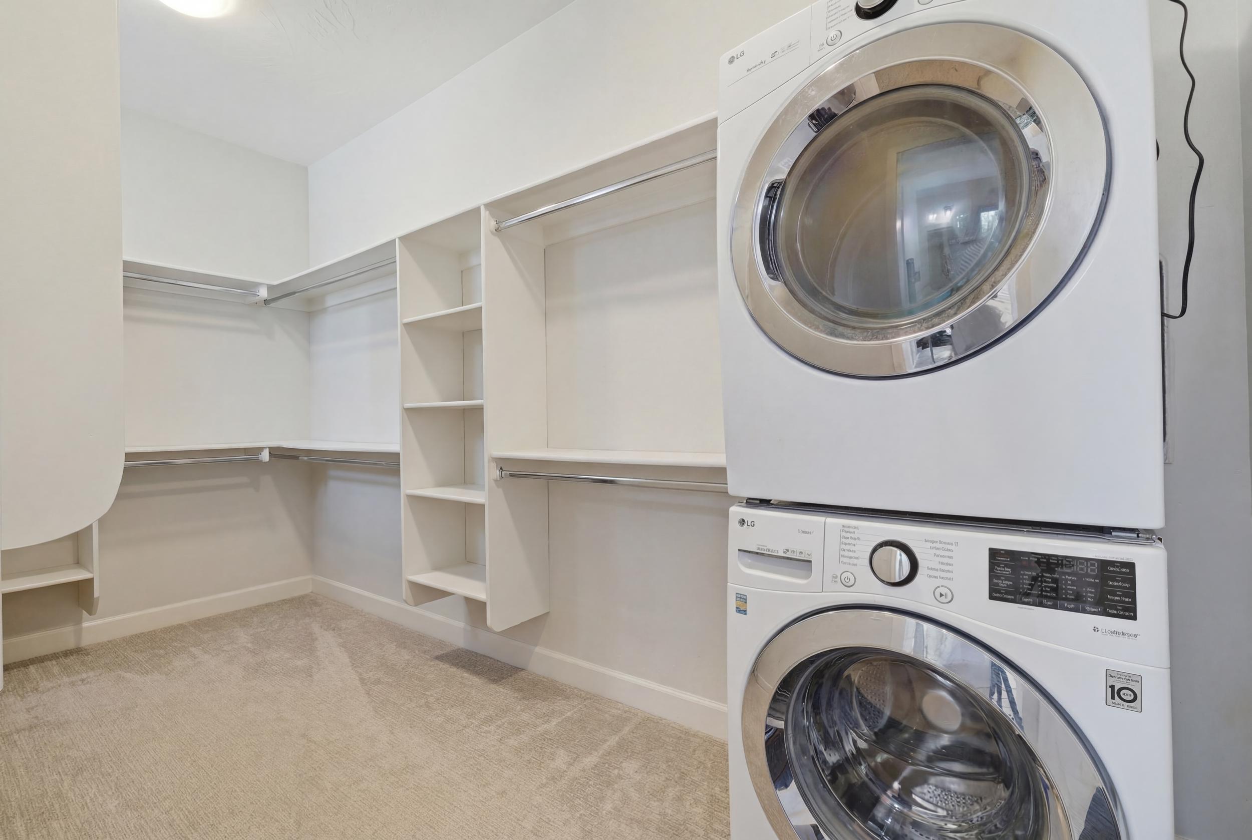 Walk-in closet featuring white built-in shelving, hanging rods, light-toned carpet flooring, and a stacked washer and dryer unit