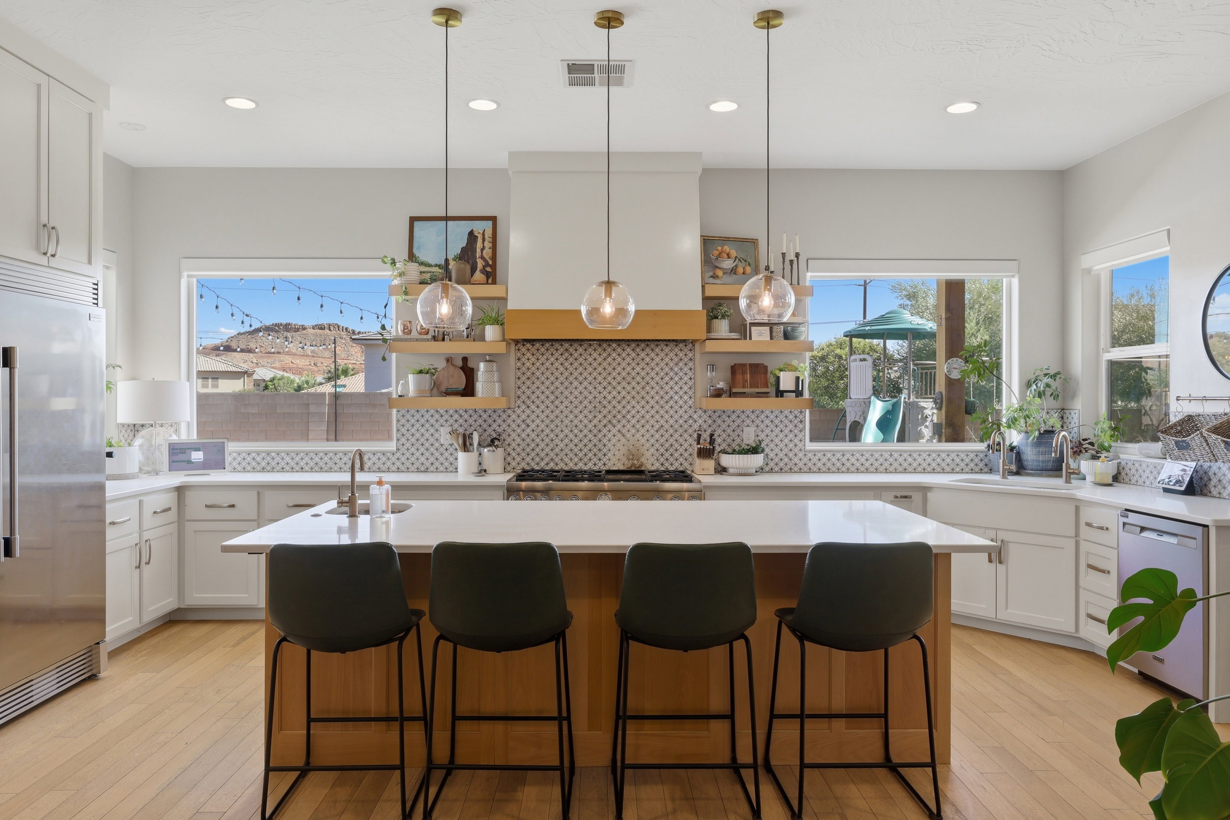 Spacious kitchen featuring an expansive central island, white cabinetry, integrated stainless steel refrigerator, patterned tile backsplash, and light wood-finish flooring