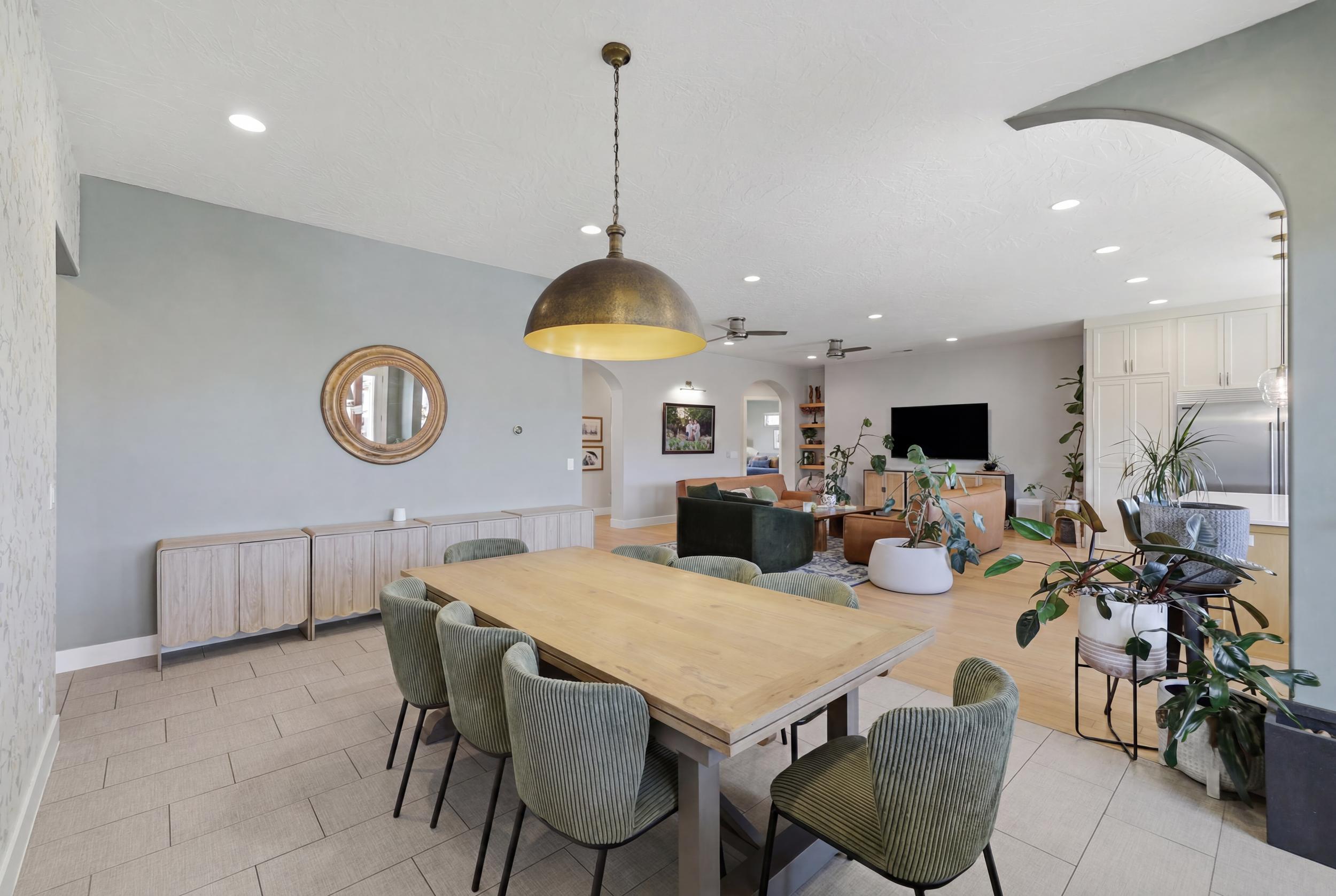 Open-concept living space featuring a dining area with tile flooring and a statement pendant light, transitioning to a living room with wood-finish flooring
