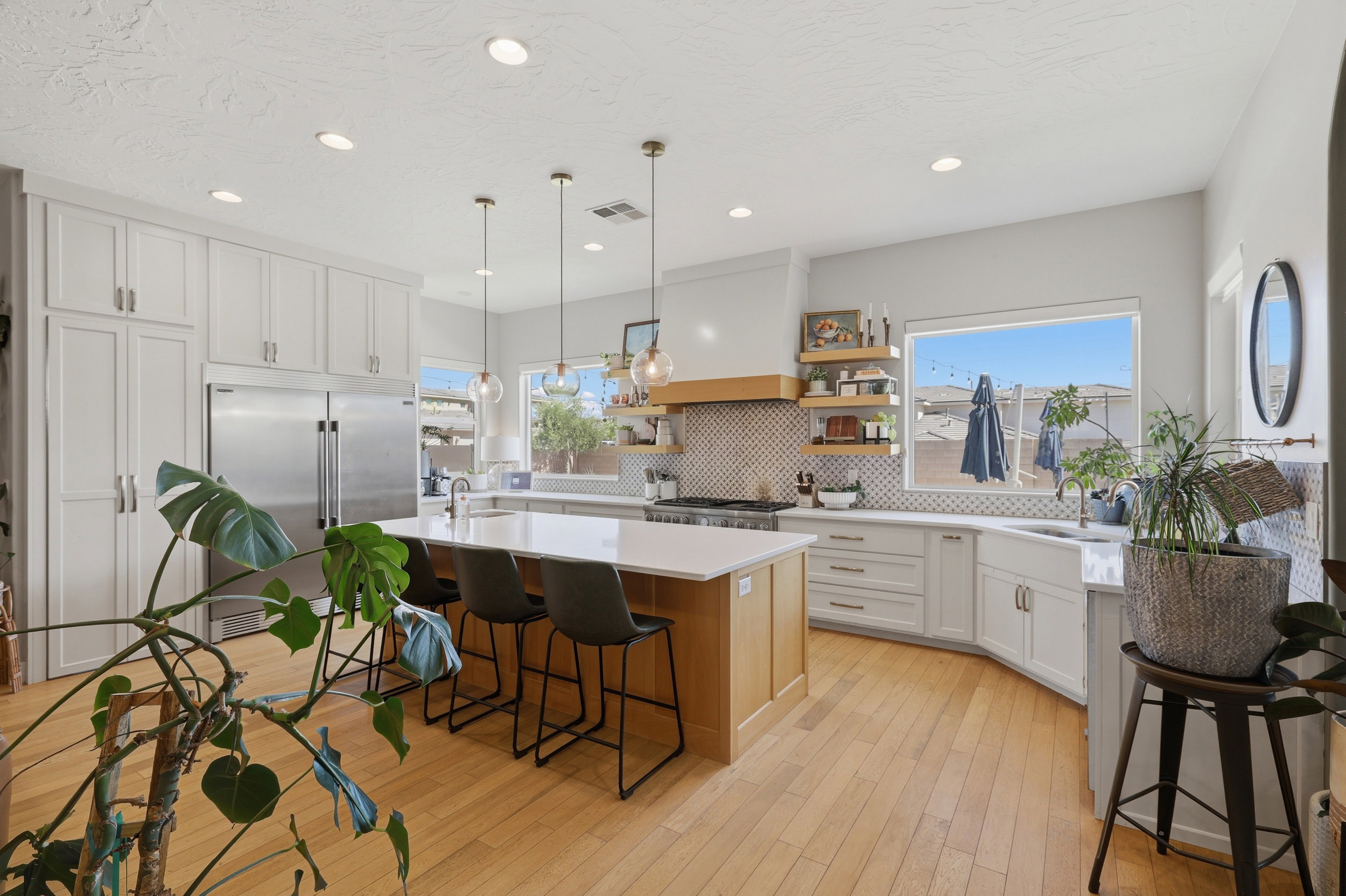 Gourmet kitchen featuring a large central island with seating, stainless steel appliances, extensive white cabinetry, light wood-finish flooring, and a patterned tile backsplash