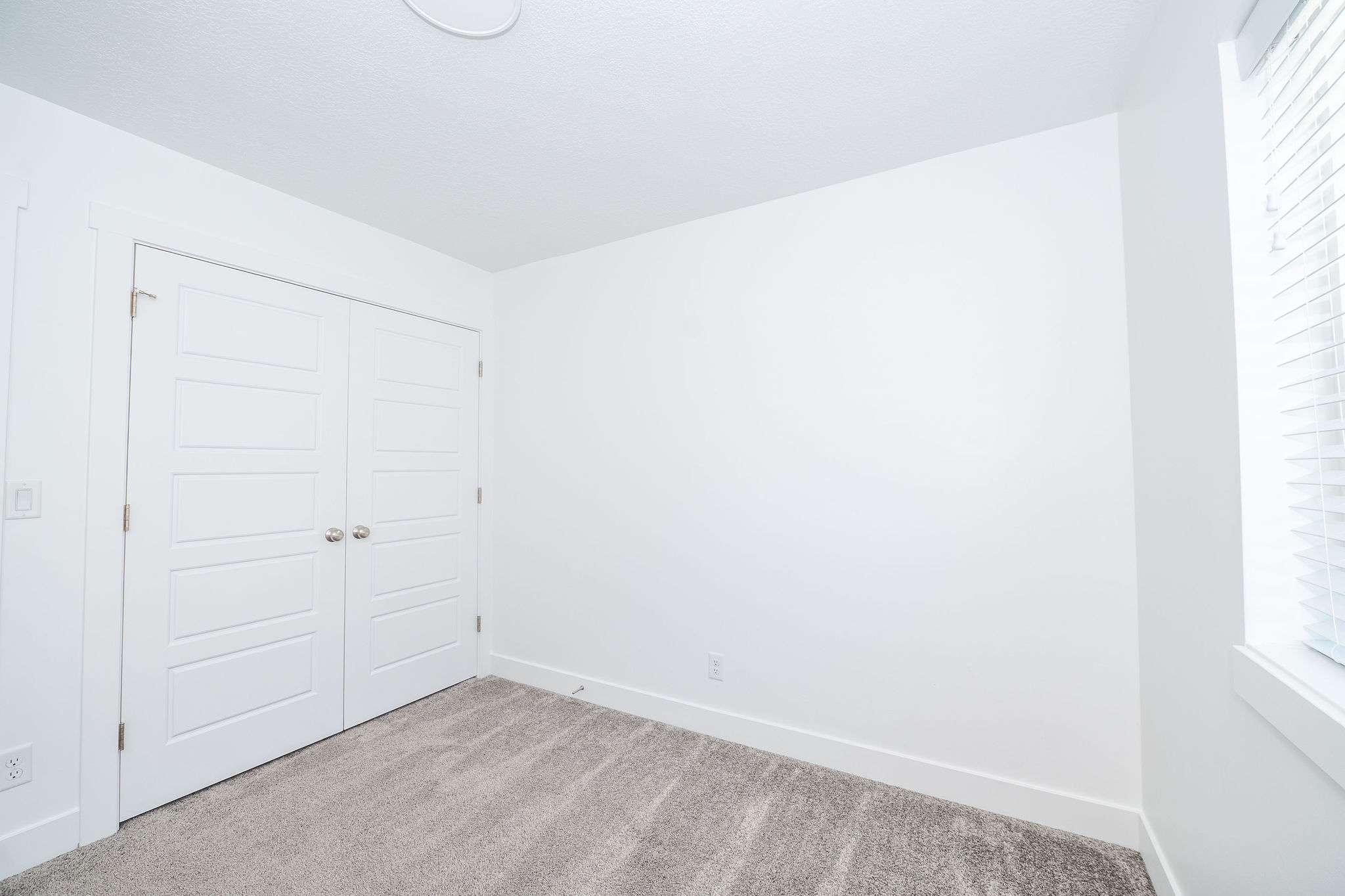 Carpeted interior space featuring white walls and a pair of white paneled bifold doors with chrome hardware