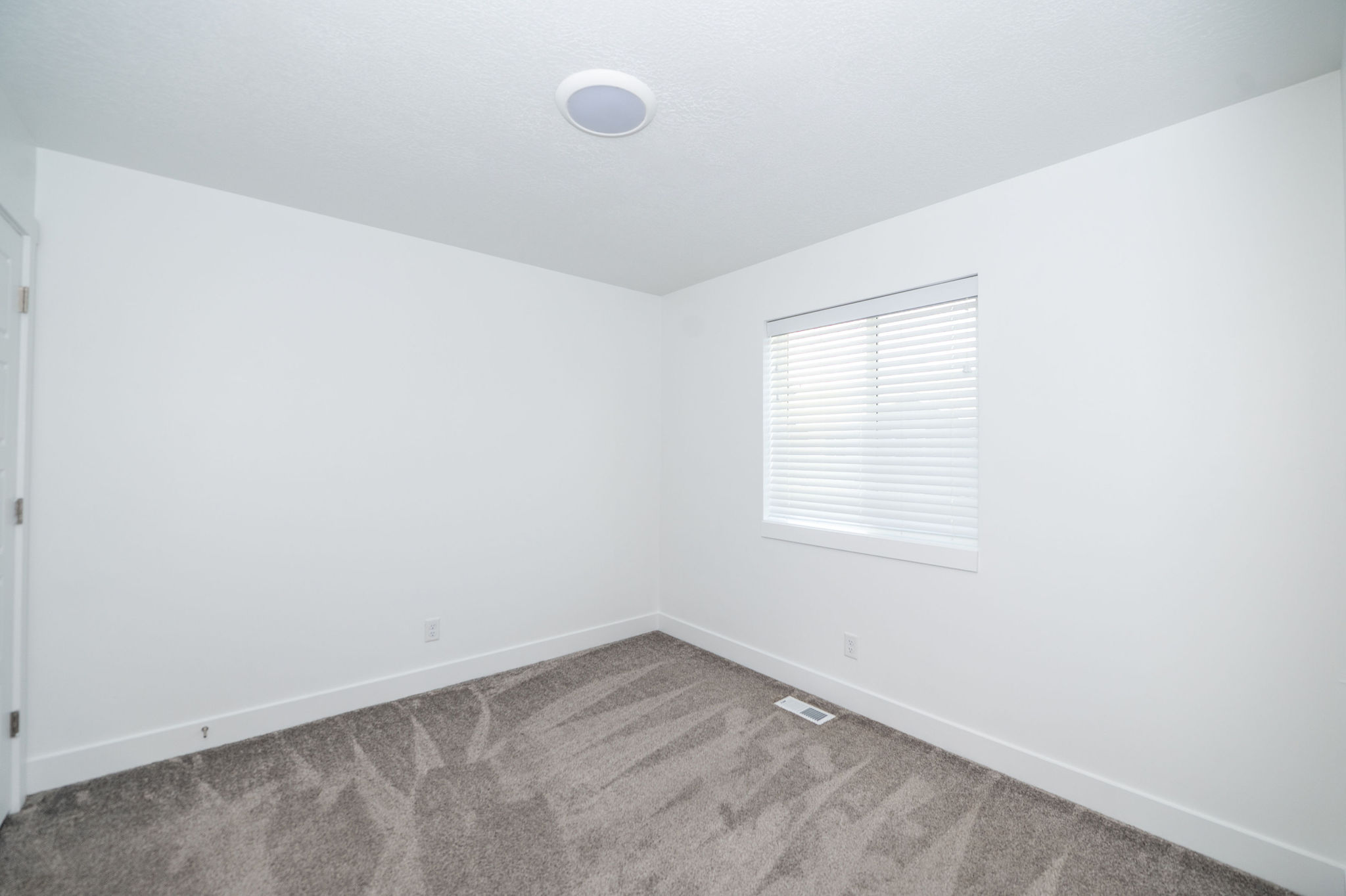 Carpeted room featuring a single window with blinds, white walls, white trim, and a ceiling-mounted light fixture