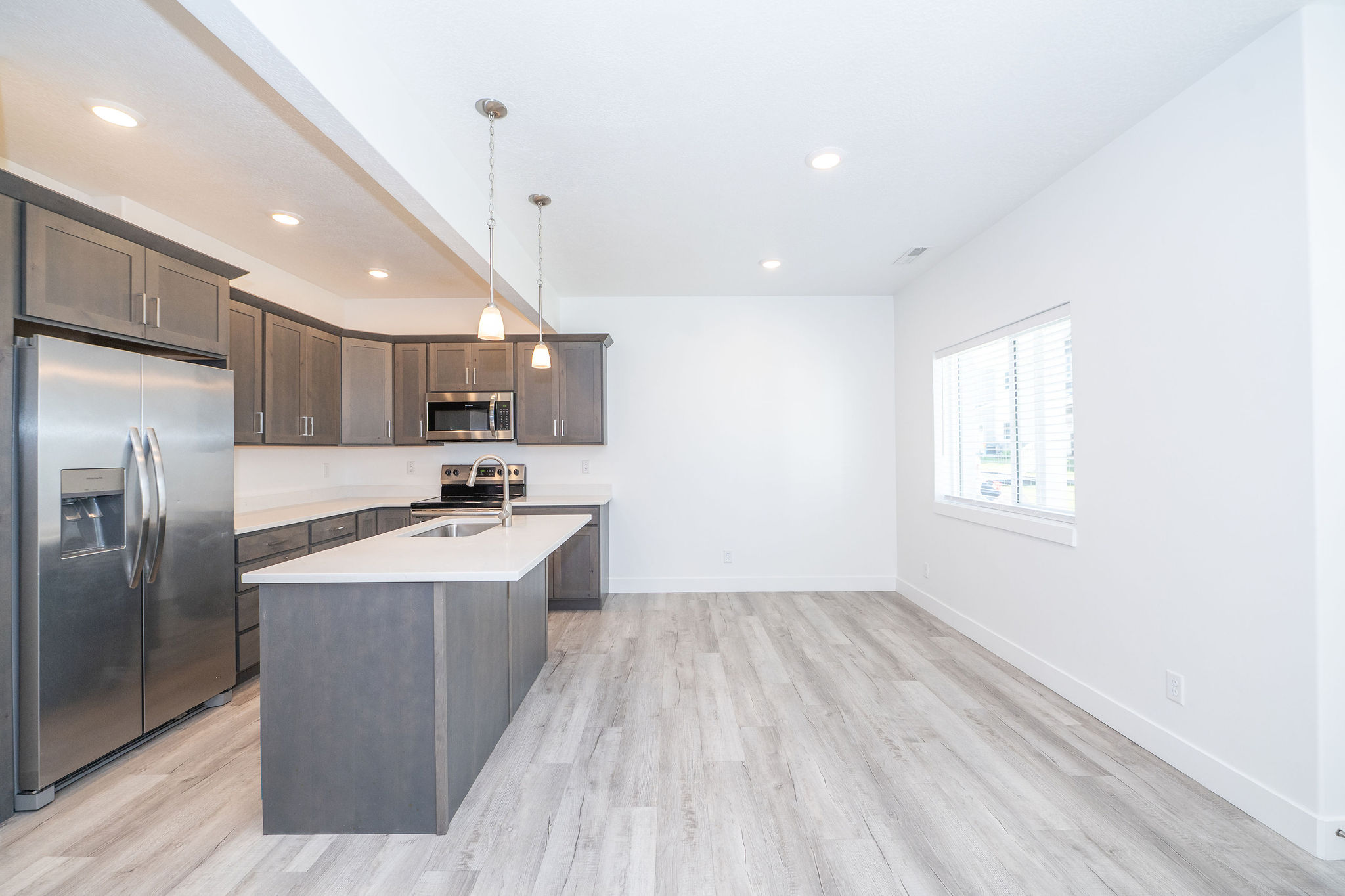 Open-concept kitchen featuring gray cabinetry, stainless steel appliances, a central island with an undermount sink, pendant lighting, and wood-finish flooring
