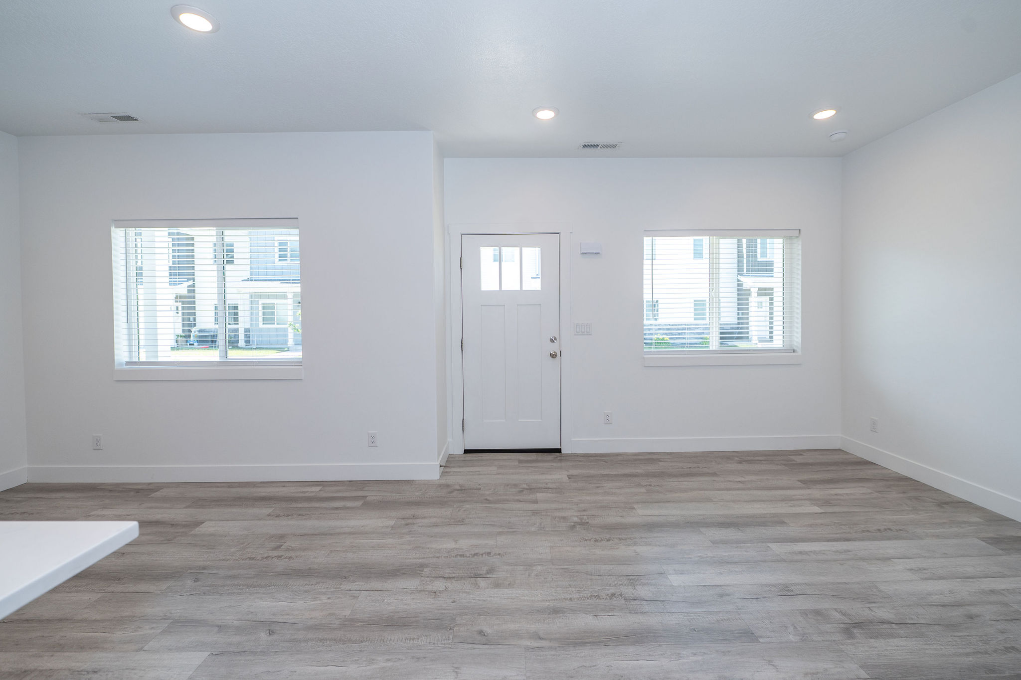 Entryway featuring a white paneled door with glass inserts, flanked by two windows with blinds