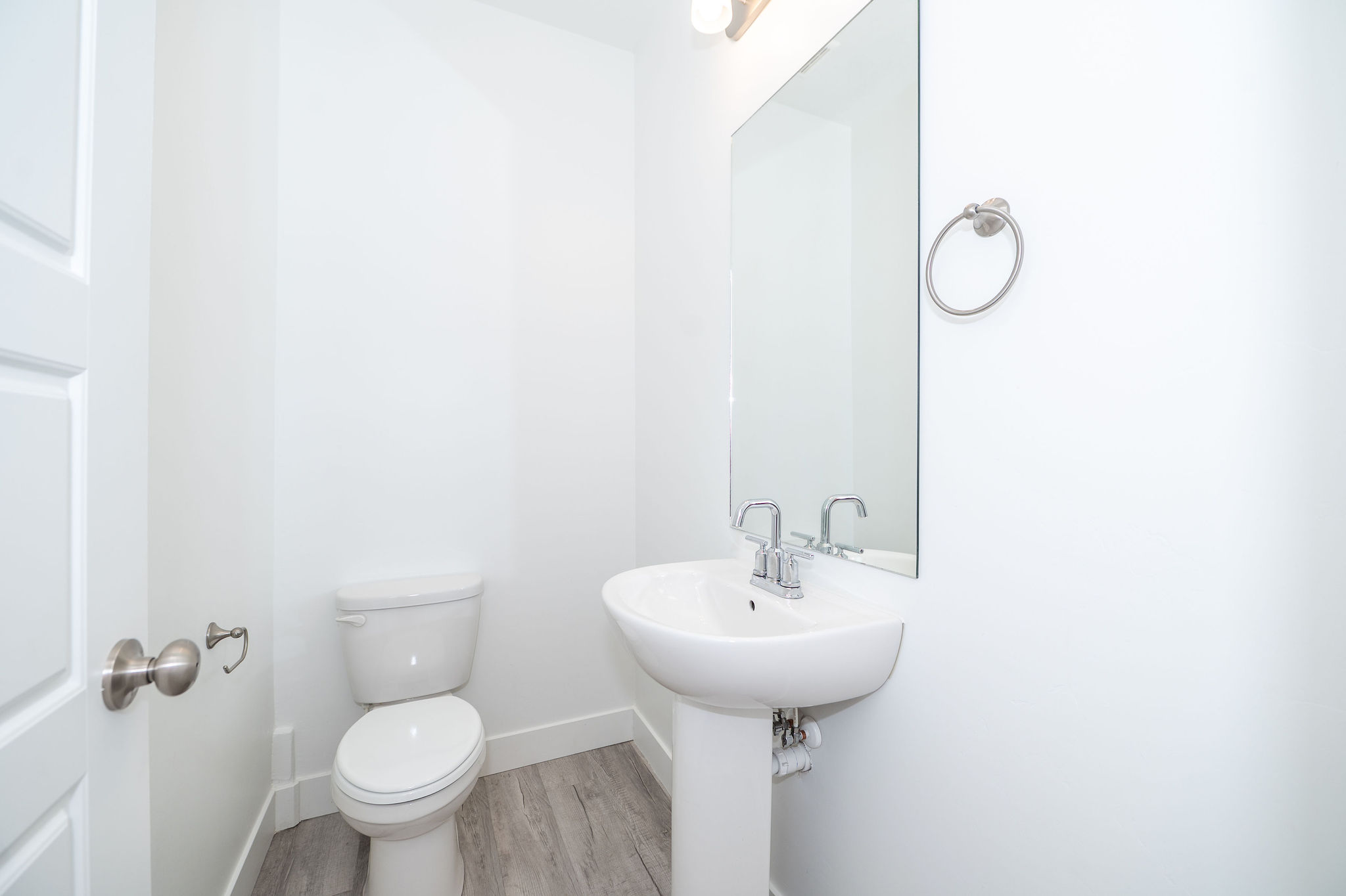 Powder room featuring a pedestal sink with chrome fixtures, a wall-mounted mirror, and wood-finish flooring