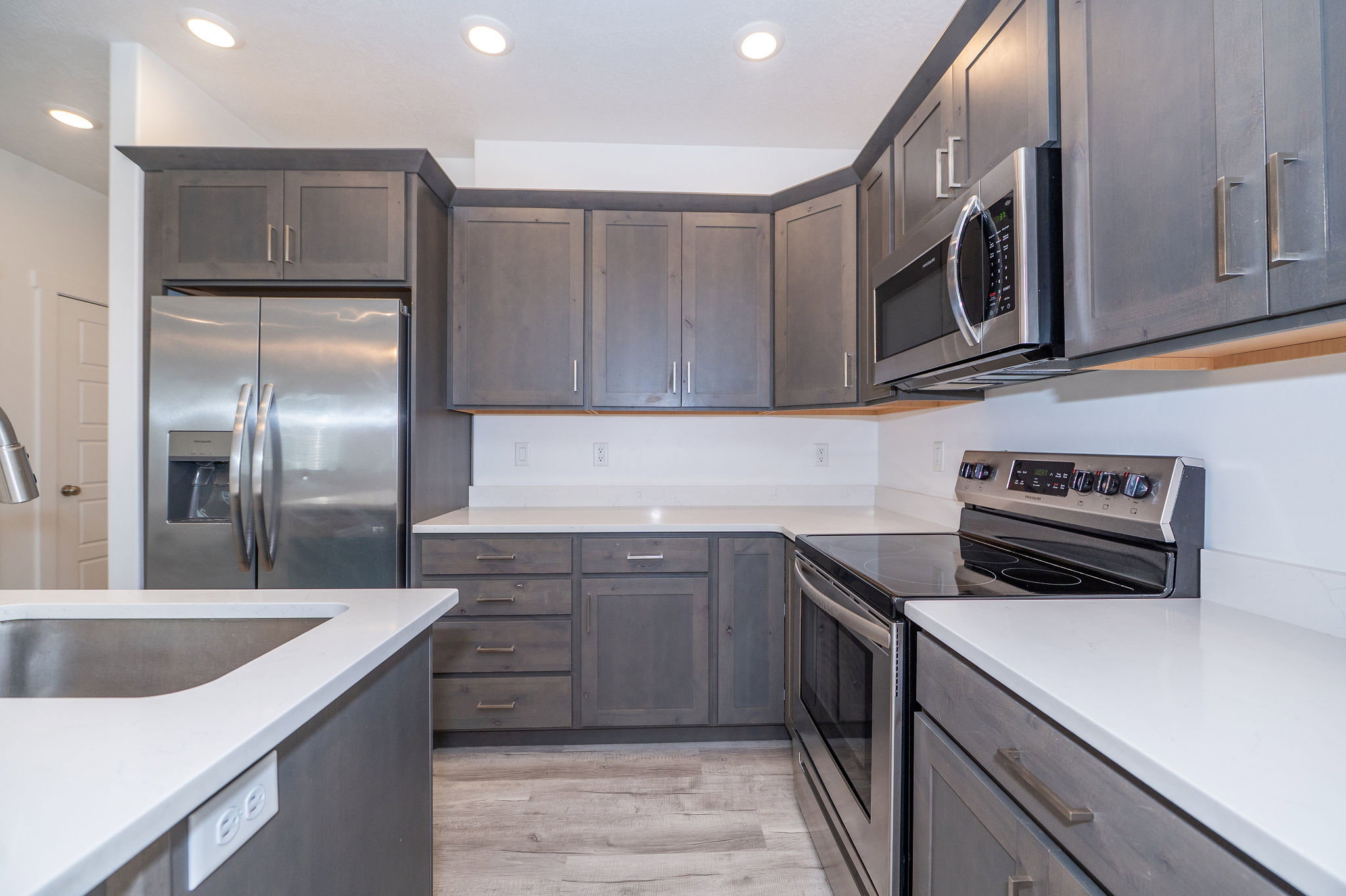 Kitchen featuring dark wood-finish cabinetry, white solid surface countertops, stainless steel appliances, and recessed ceiling lighting