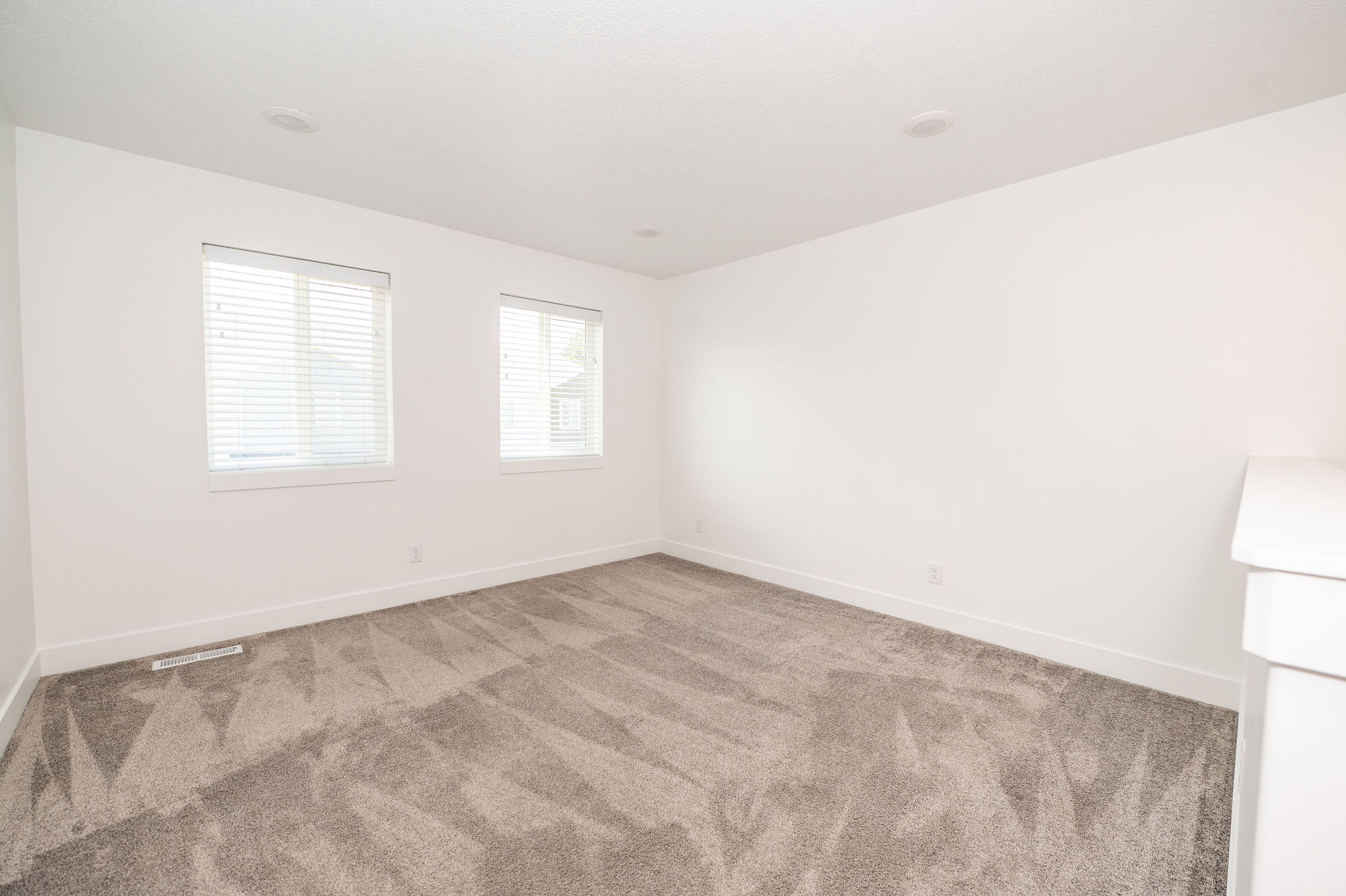 Spacious room featuring neutral carpeting, two windows with blinds, recessed lighting, and crisp white walls