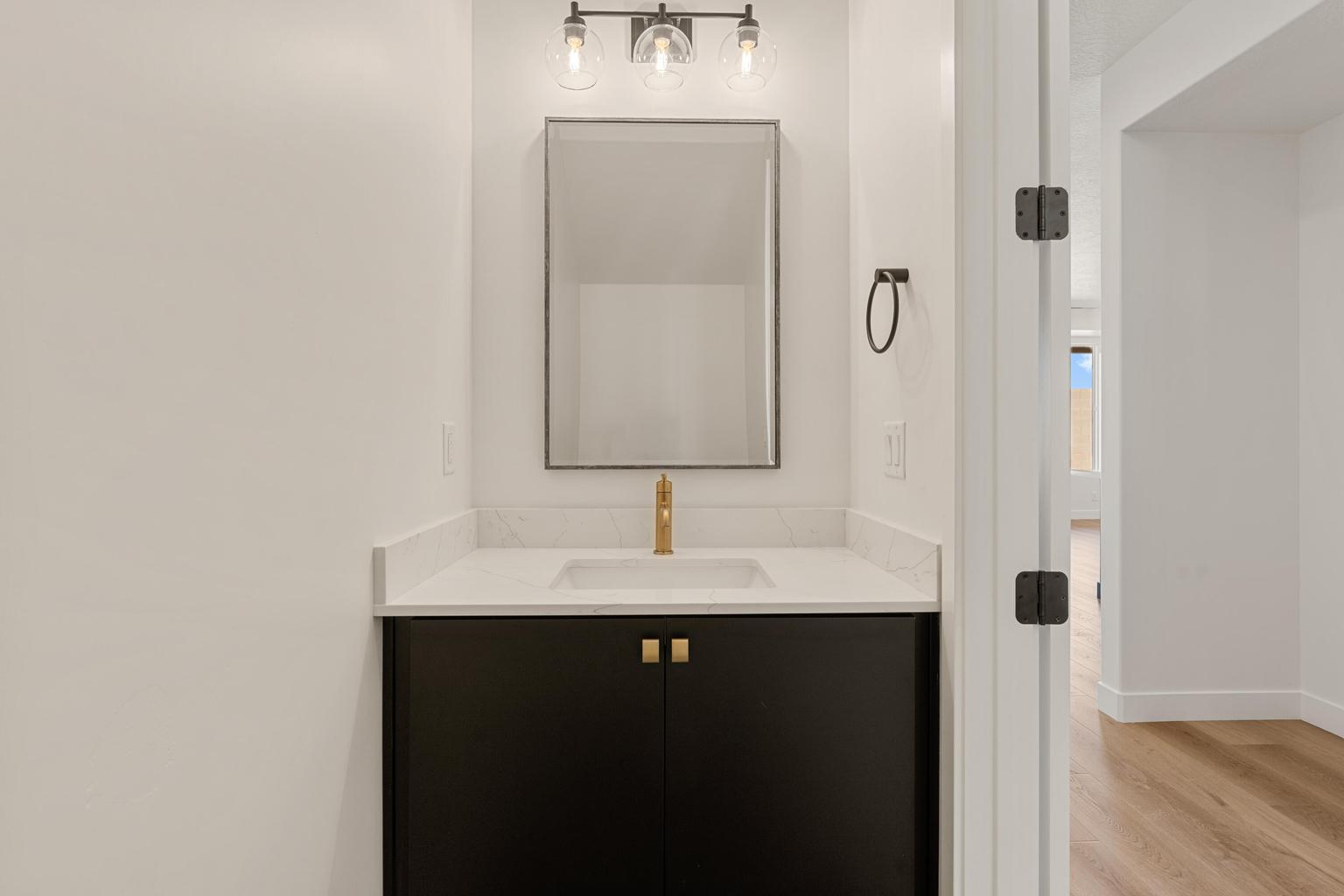 Modern vanity featuring a black cabinet, gold hardware, and a white countertop with an integrated sink
