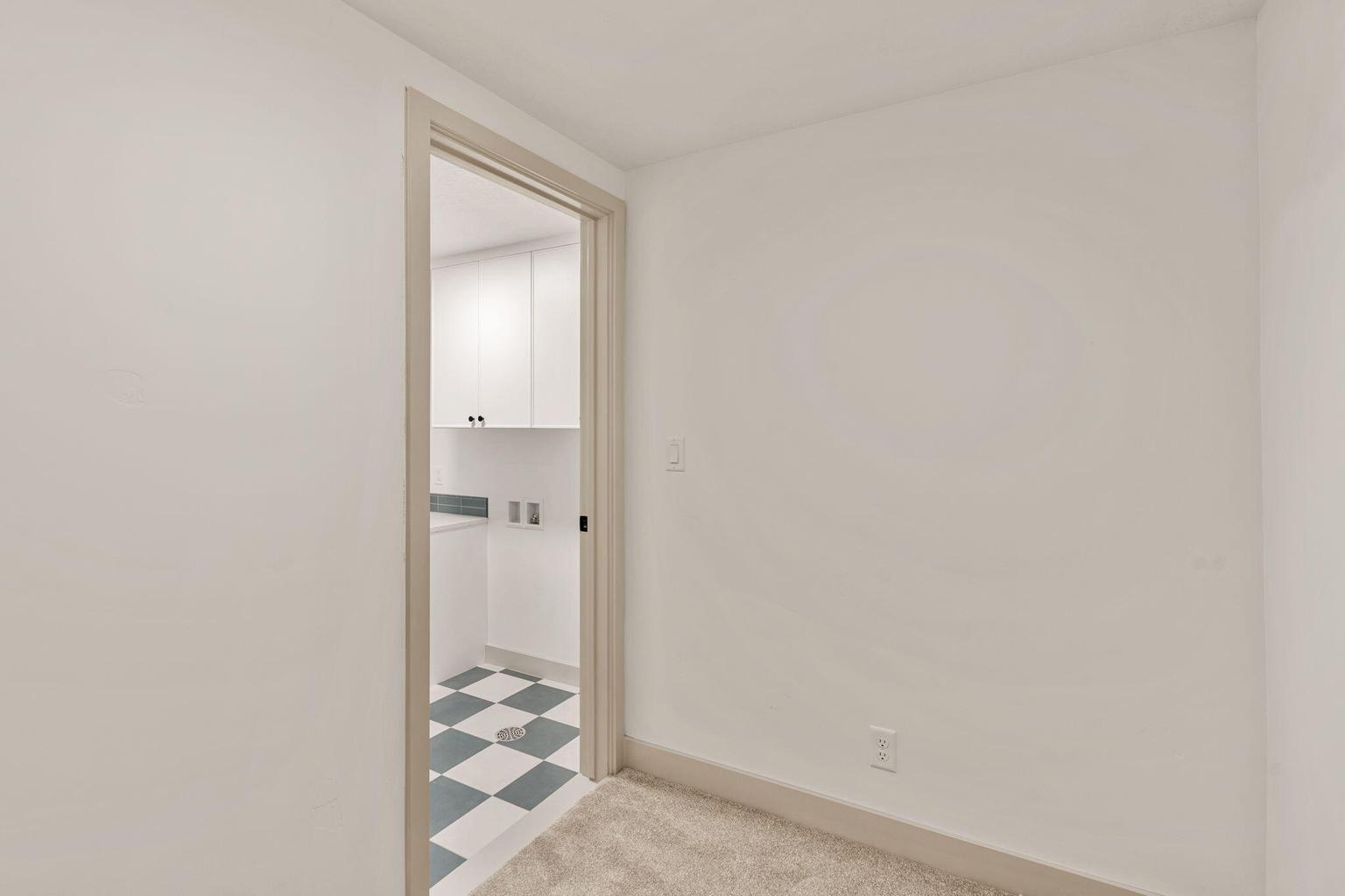 Utility room entrance with a light wood-finish door frame, featuring checkered floor tiles, white cabinetry, and a countertop space
