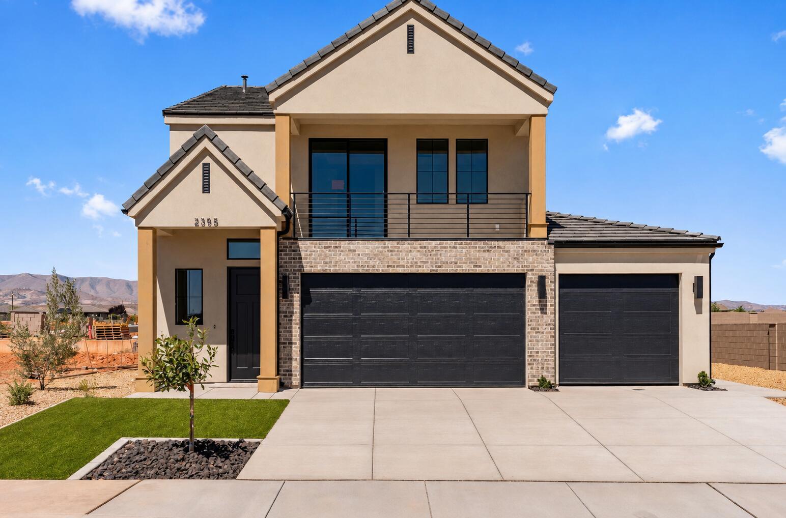 Contemporary two-story residence featuring a stucco and brick exterior, dark garage doors, and a second-story balcony with metal railing